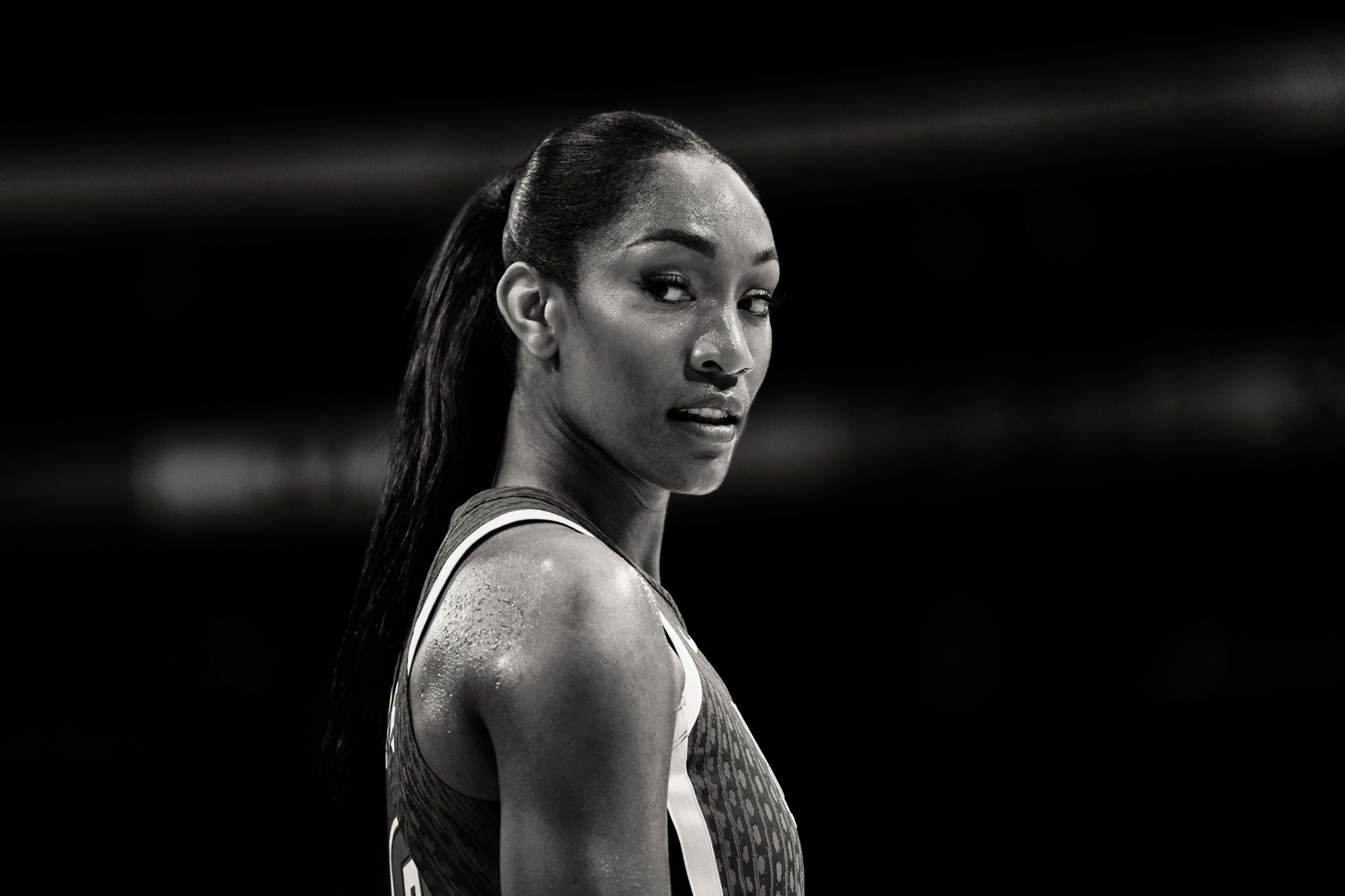 Black and white side angled view of A'ja Wilson looking over her shoulder at a basketball stadium.