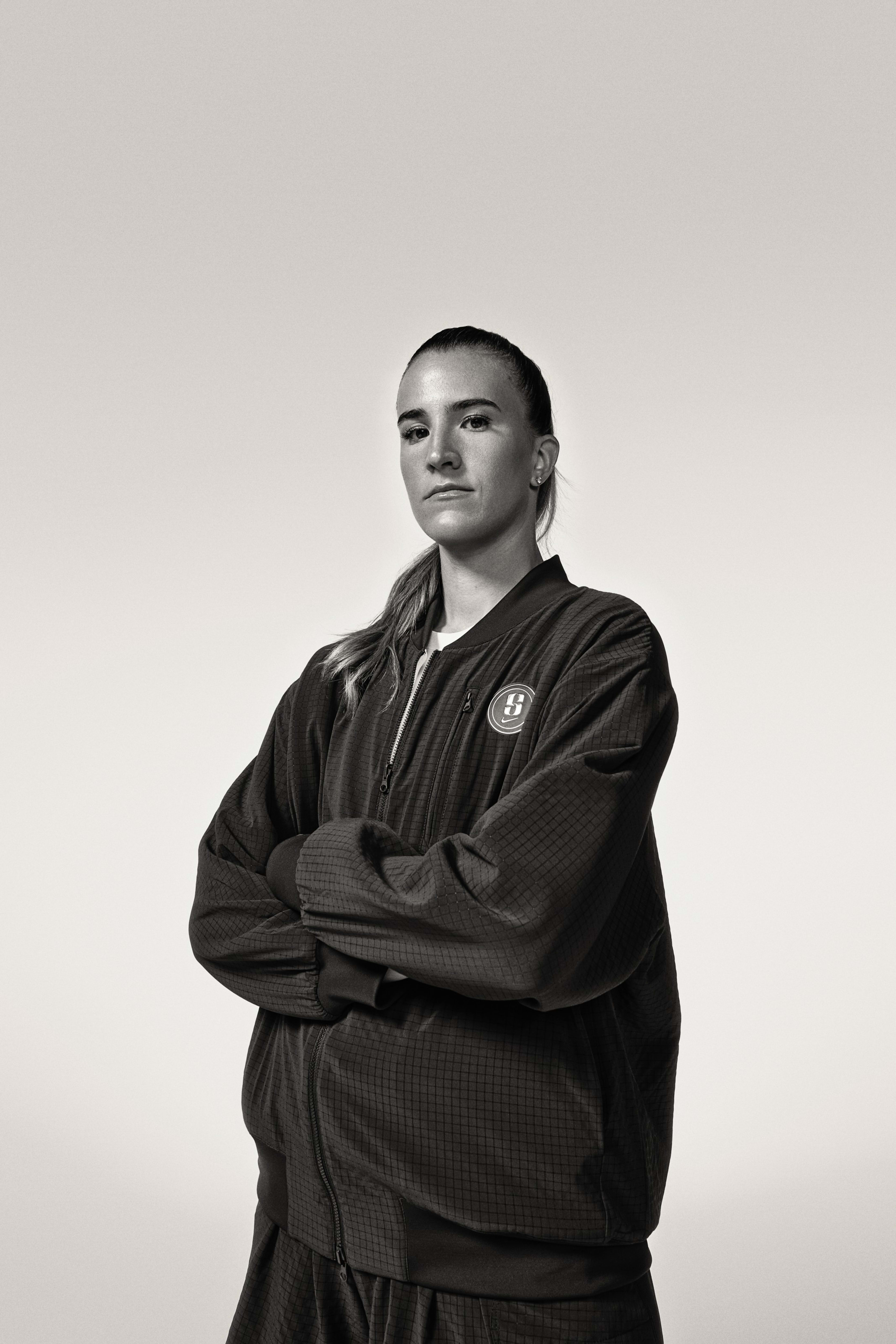 Black and white portrait of Sabrina Ionescu in the Sabrina reversible basketball jacket. She looks directly at the camera with her arms crossed.