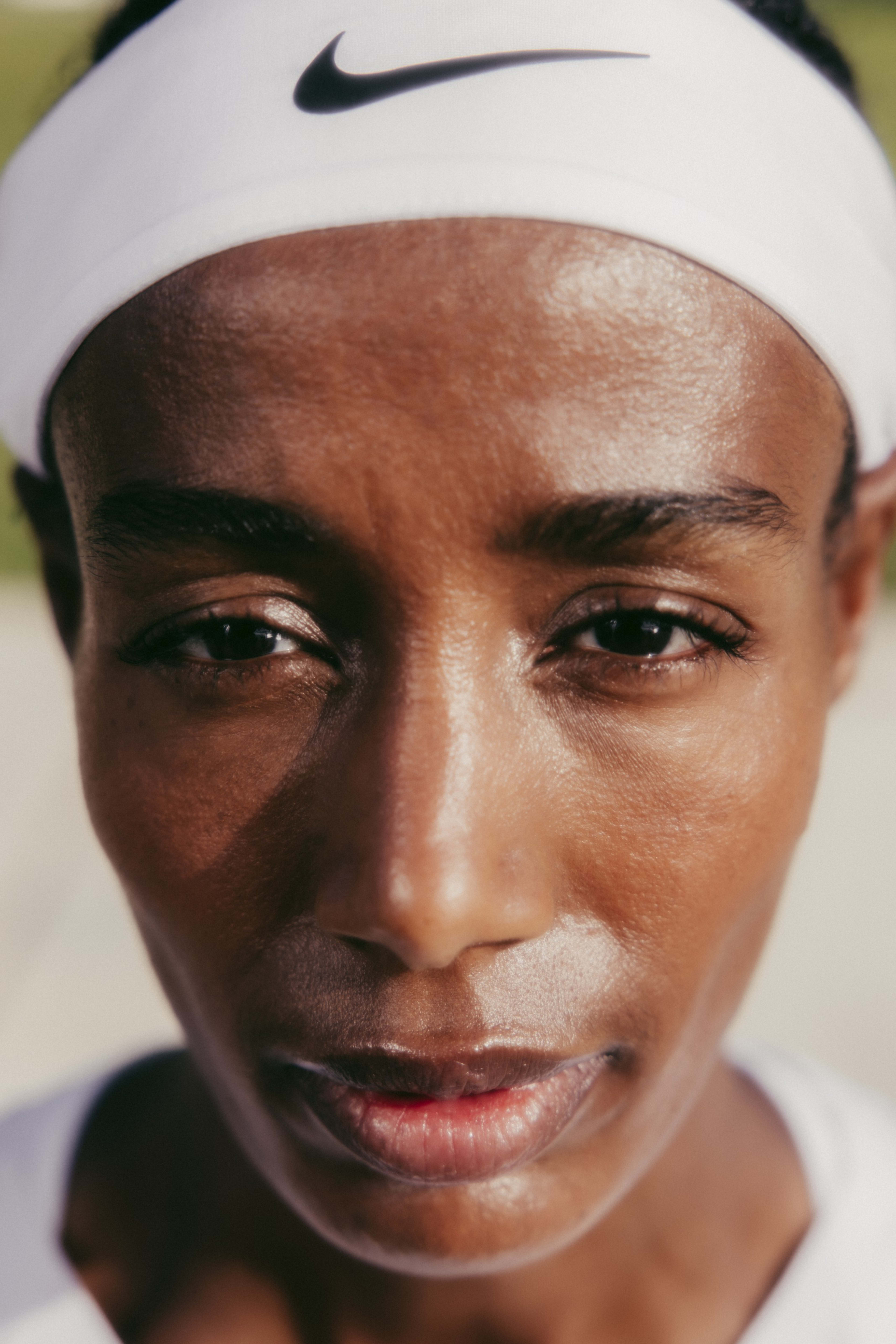 Close up head shot of Sifan Hassan wearing a white Nike headband with a black Swoosh.  Sifan's face is partially in shadow.