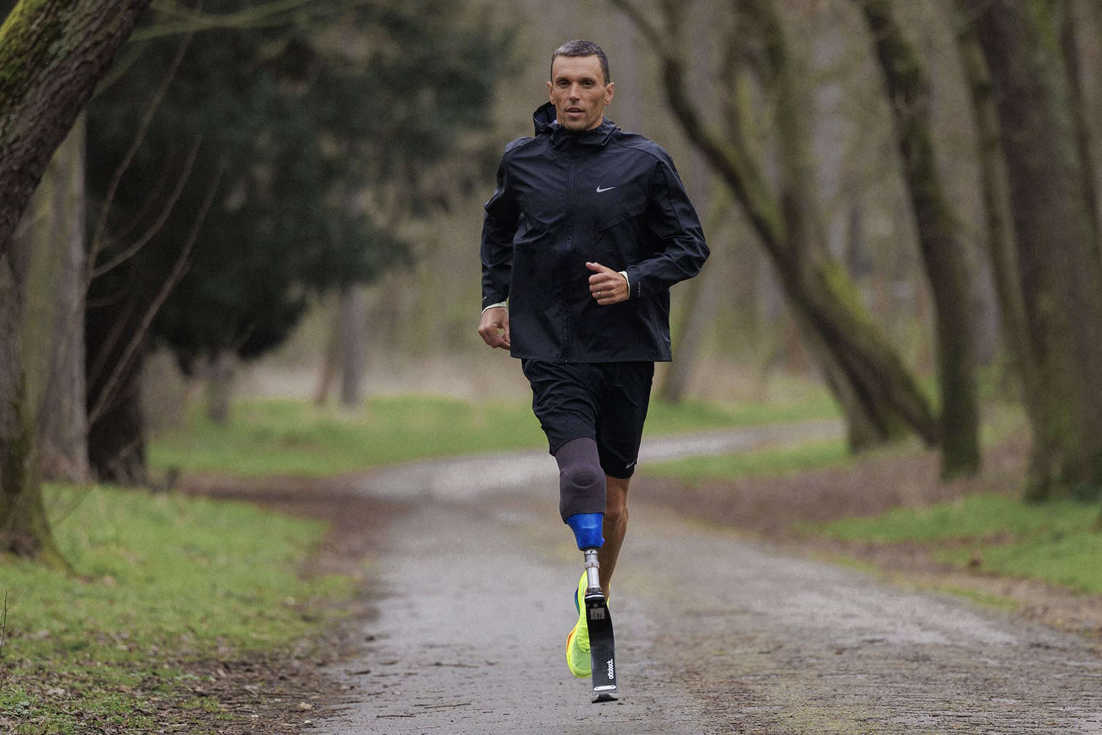 Alexis Hanquinquant runs down a forested pathway in black Nike Stride shorts and Nike Miler jacket. He strides in the Nike Alphafly 3 in bright Volt green and his triathlon blade.