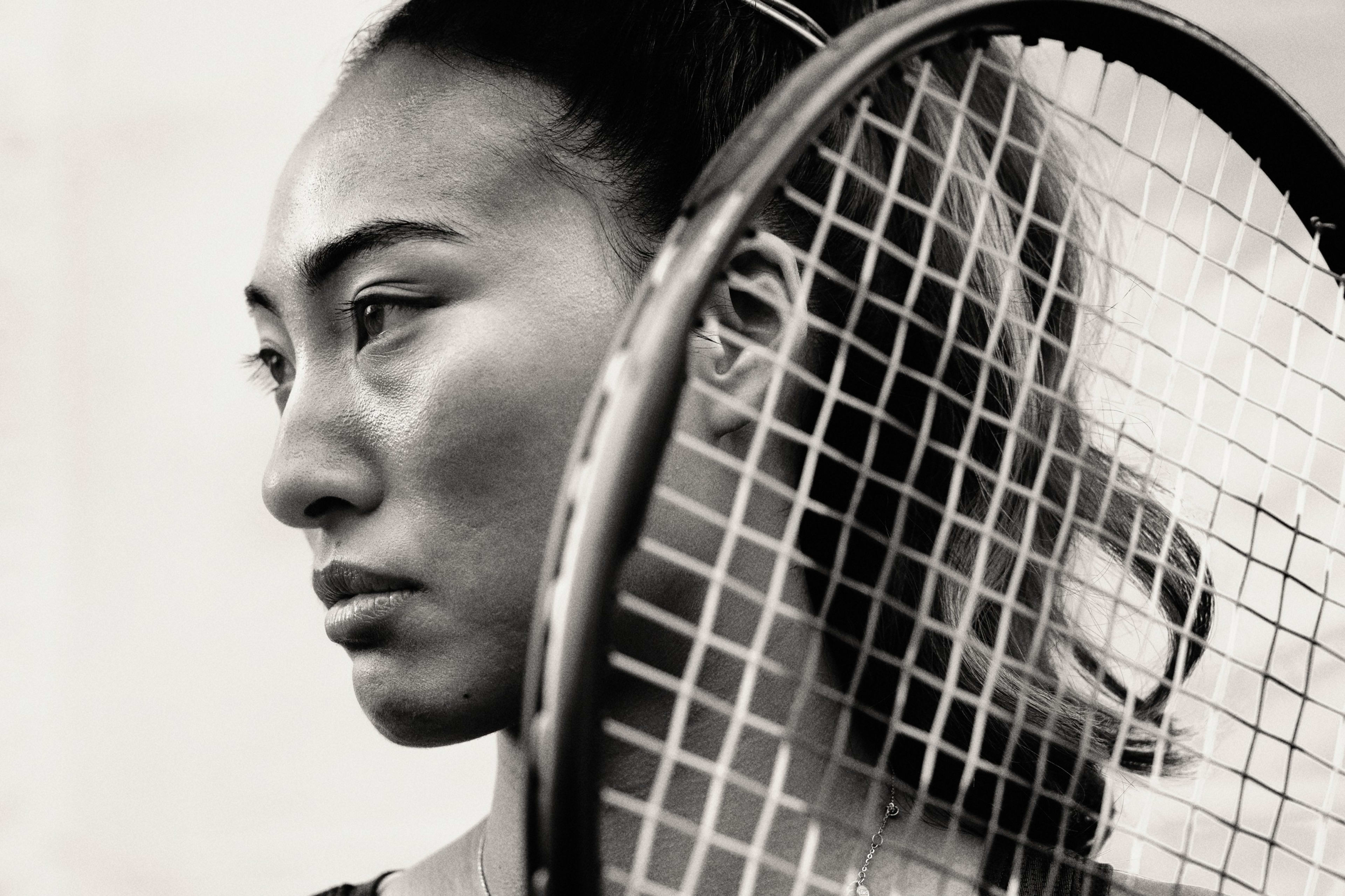 Black and white side angled close up view of Qinwen Zheng with a determined expression holding a tennis racket at shoulder height.