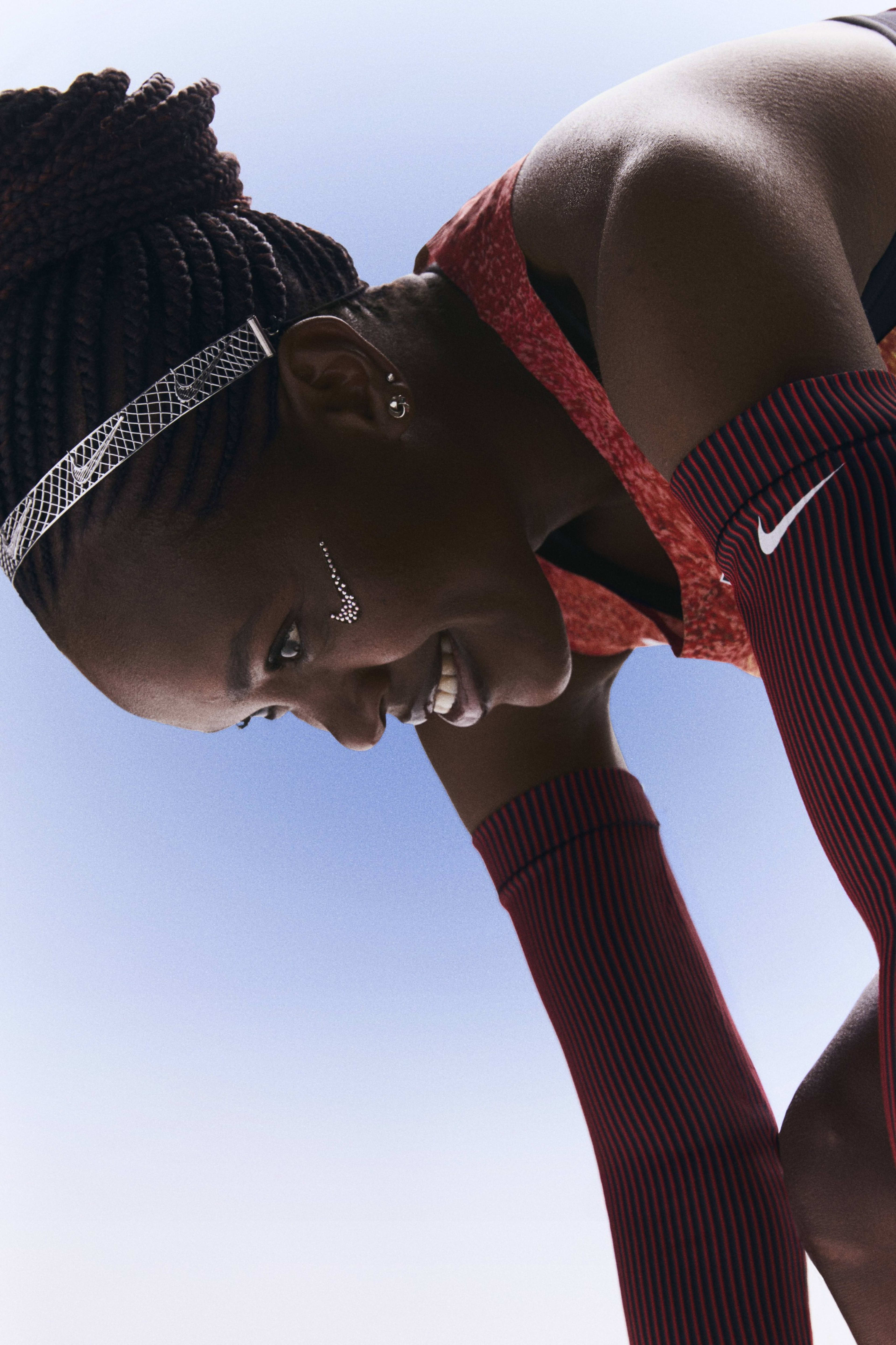 Faith Kipyegon bending forward and smiling while wearing her Kenya track and field kit uniform.