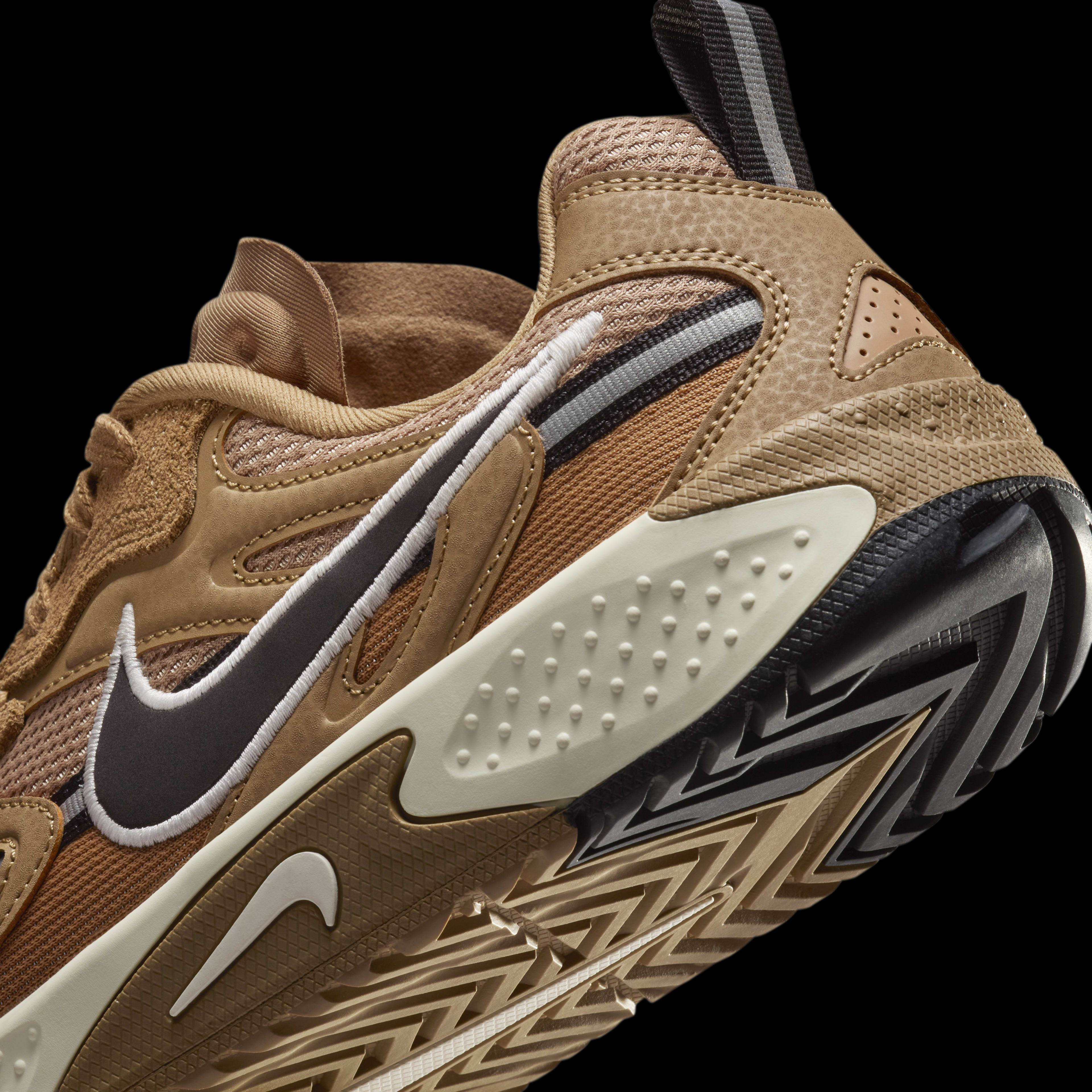 Detail side view of the Nike Jam, shown with a tan upper, tan midsole, black and tan sole, with a dark brown Swoosh surrounded by white embroidery. The shoe floats on a black background.