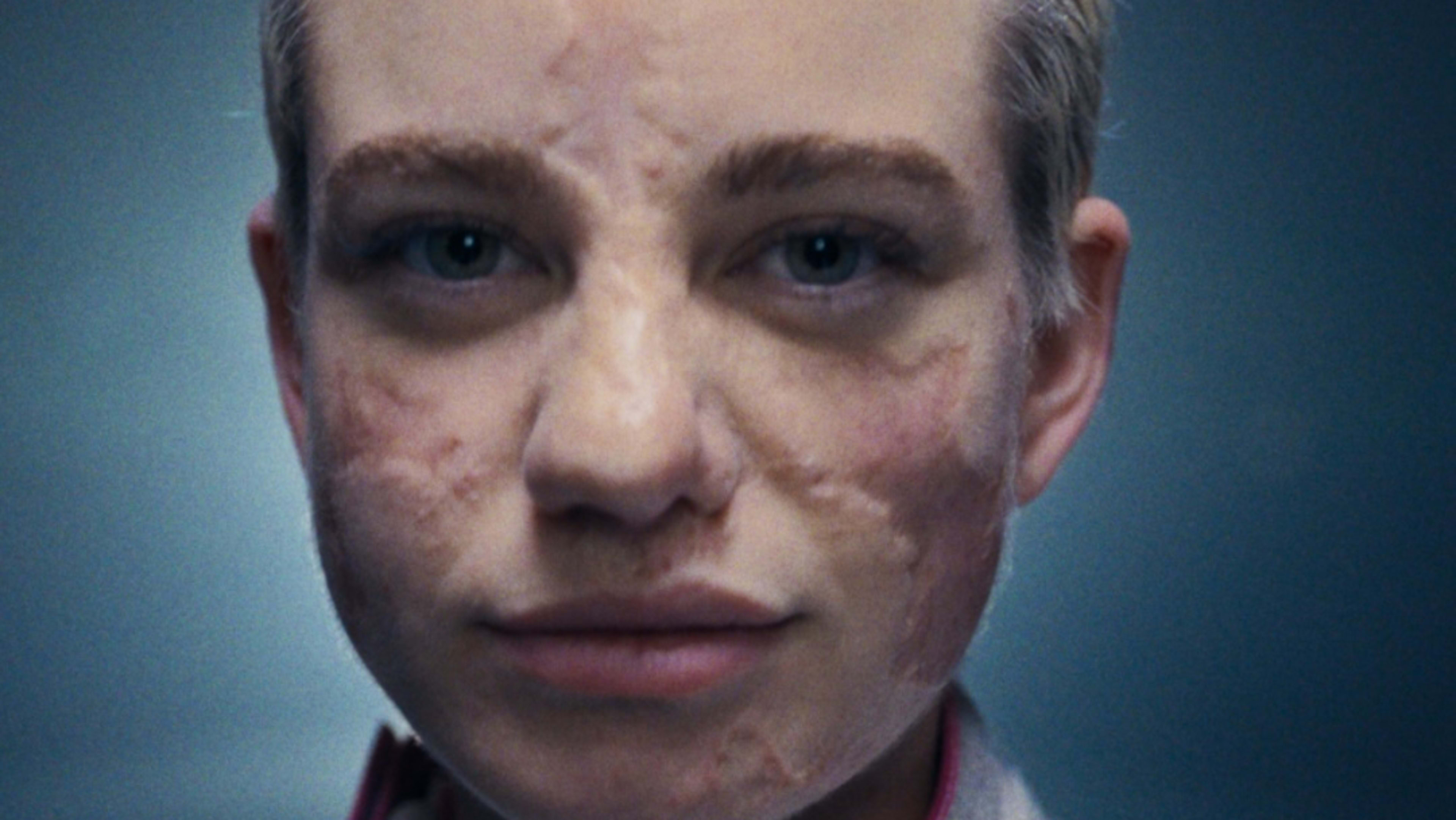 Square format, close up of Bebe Vio wearing her fencing jacket and her hair slicked back off her face. She smiles subtly at the camera, as she appears in front of a blue background.