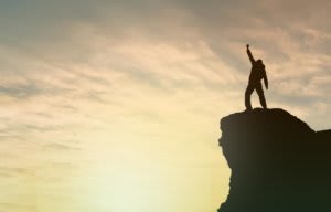 Person standing on top of a mountain, fist raised in triumph