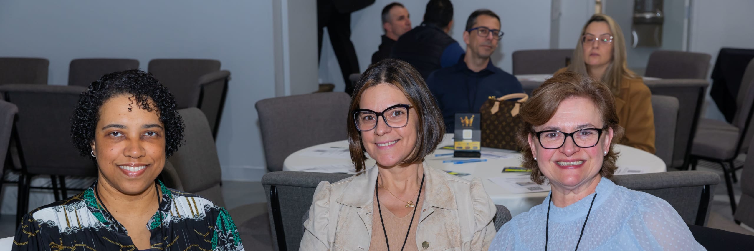 Três participantes sorriem juntas à mesa durante o encontro