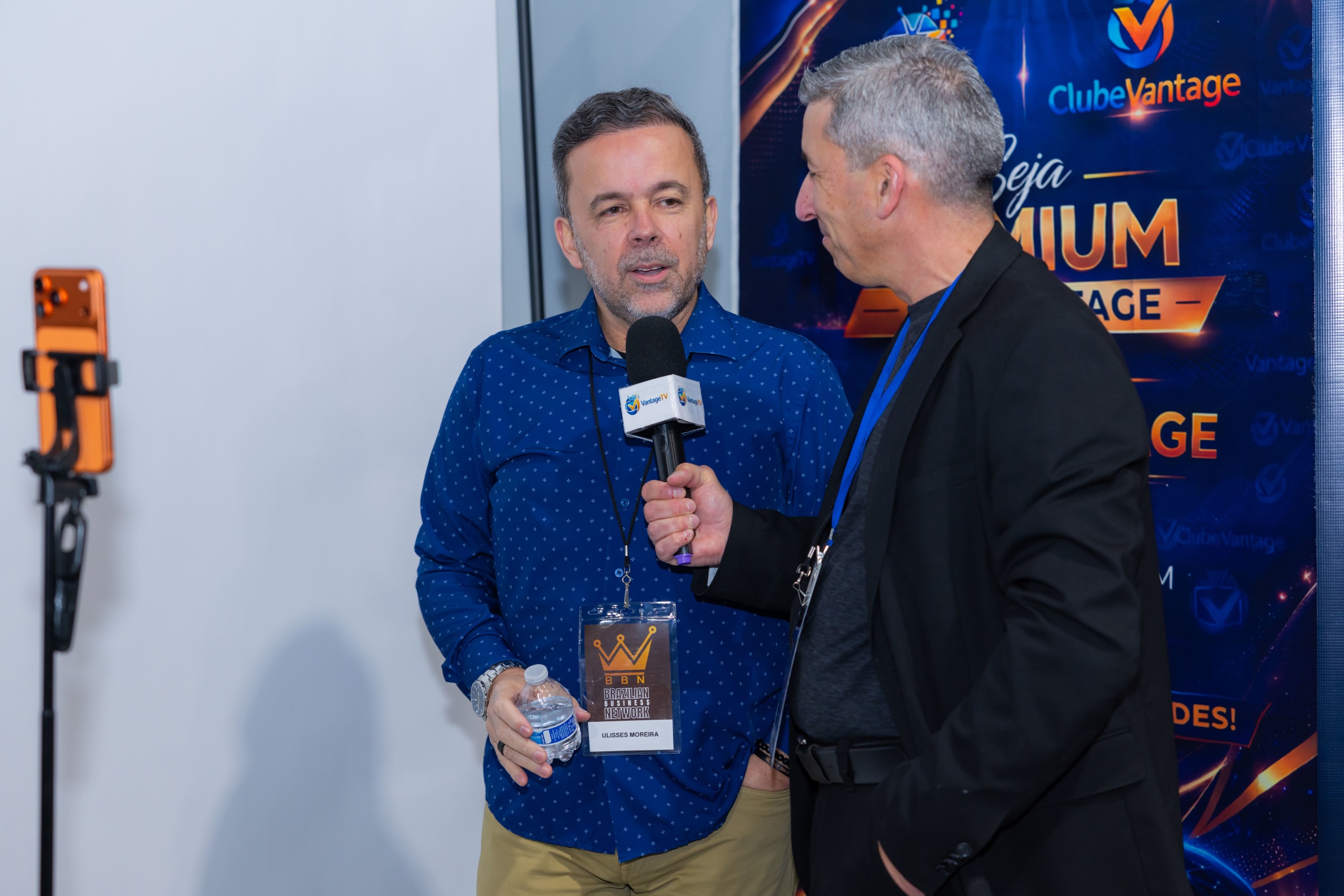 Participante do BBN dá entrevista com microfone diante do painel de um patrocinador
