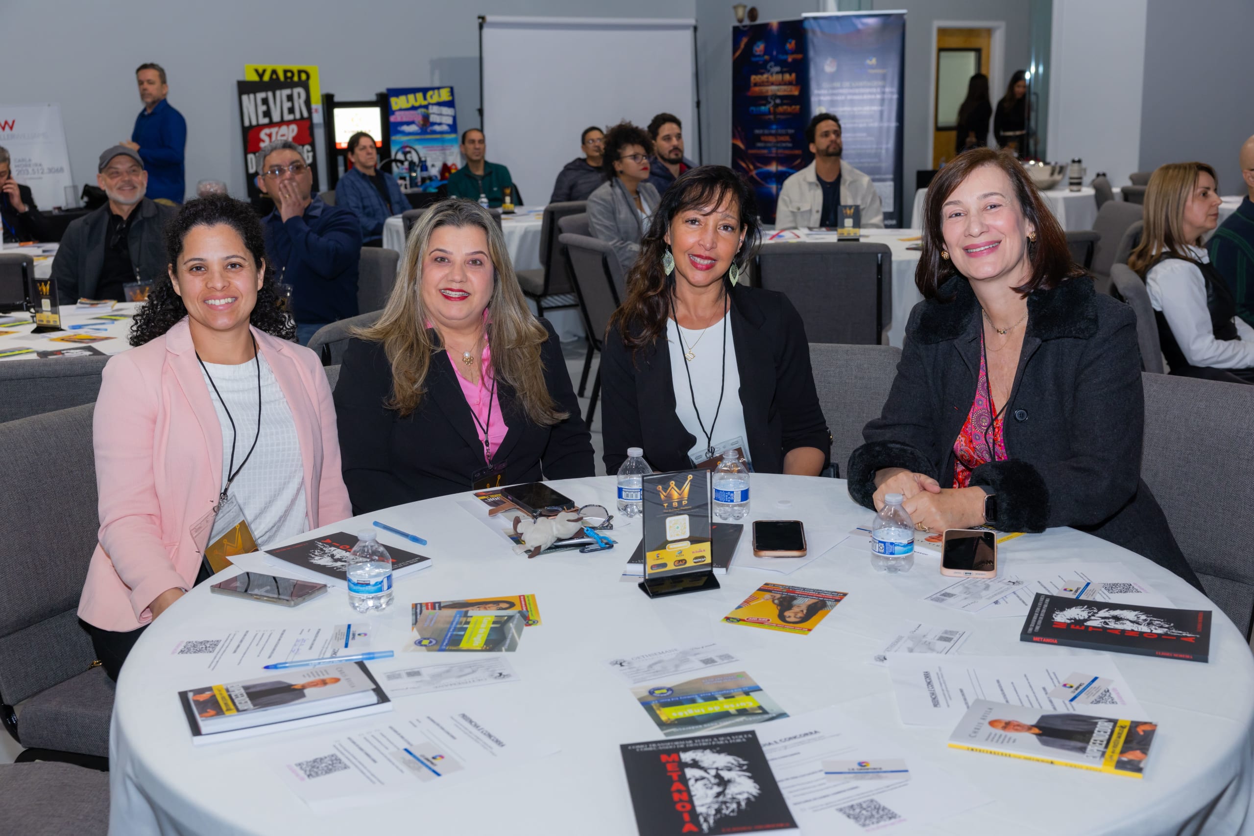 Quatro empreendedoras sorriem sentadas a uma mesa redonda, com o salão do evento ao fundo