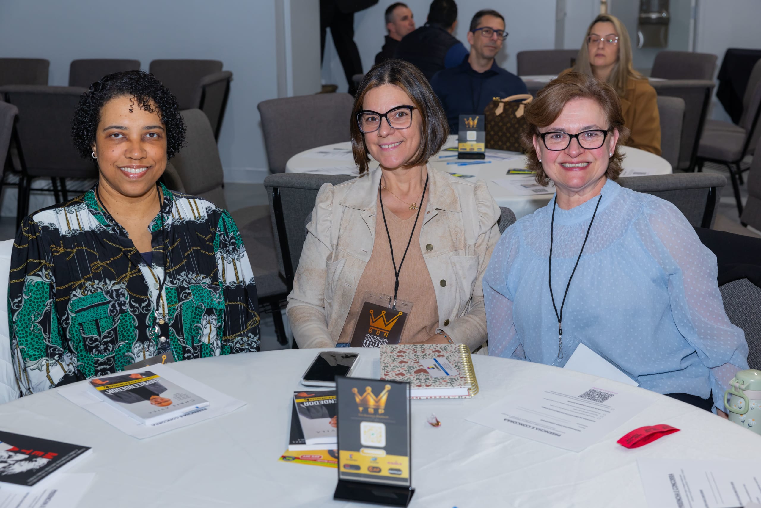 Três participantes sorriem juntas à mesa durante o encontro