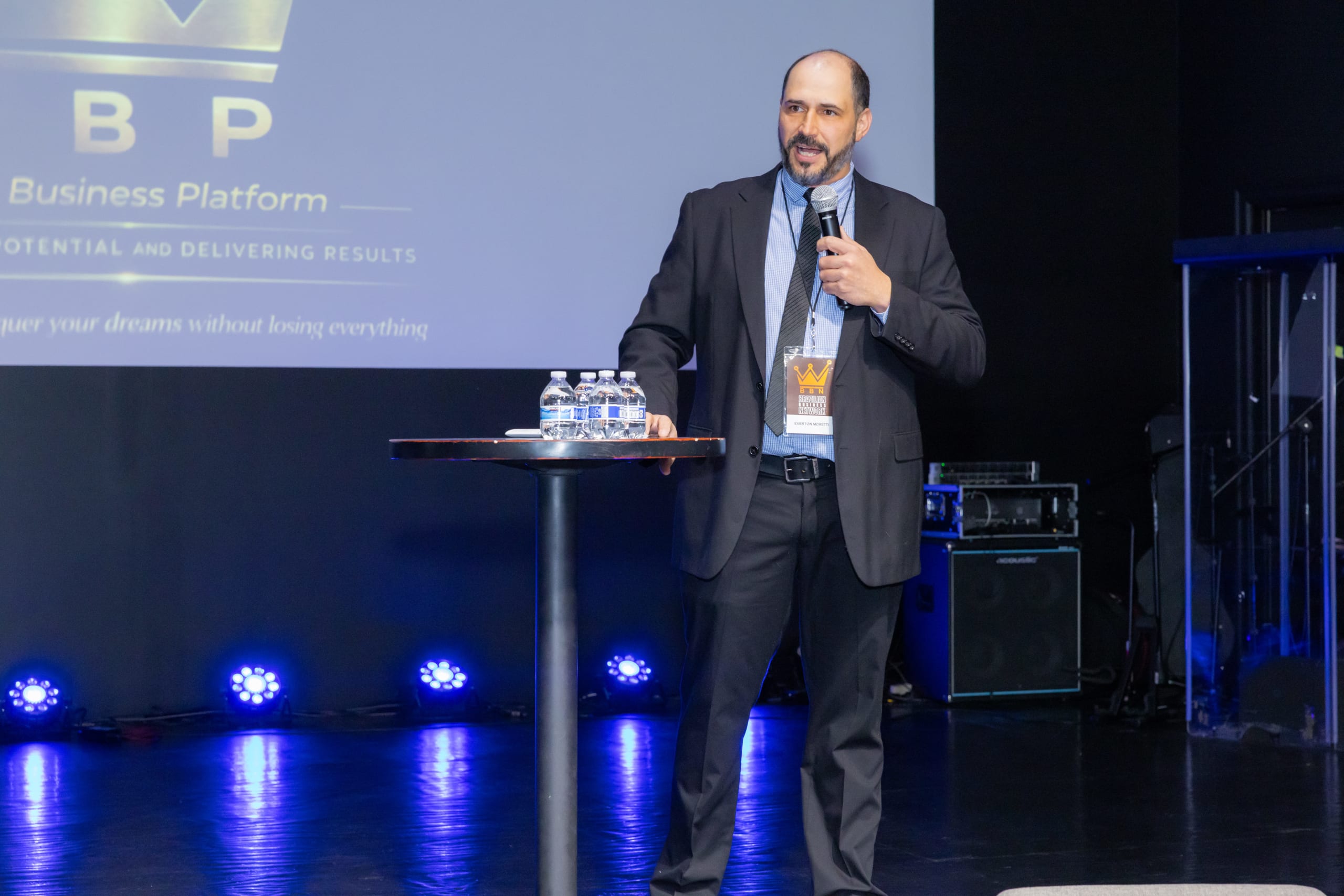 Palestrante de terno fala ao microfone no palco, diante do telão