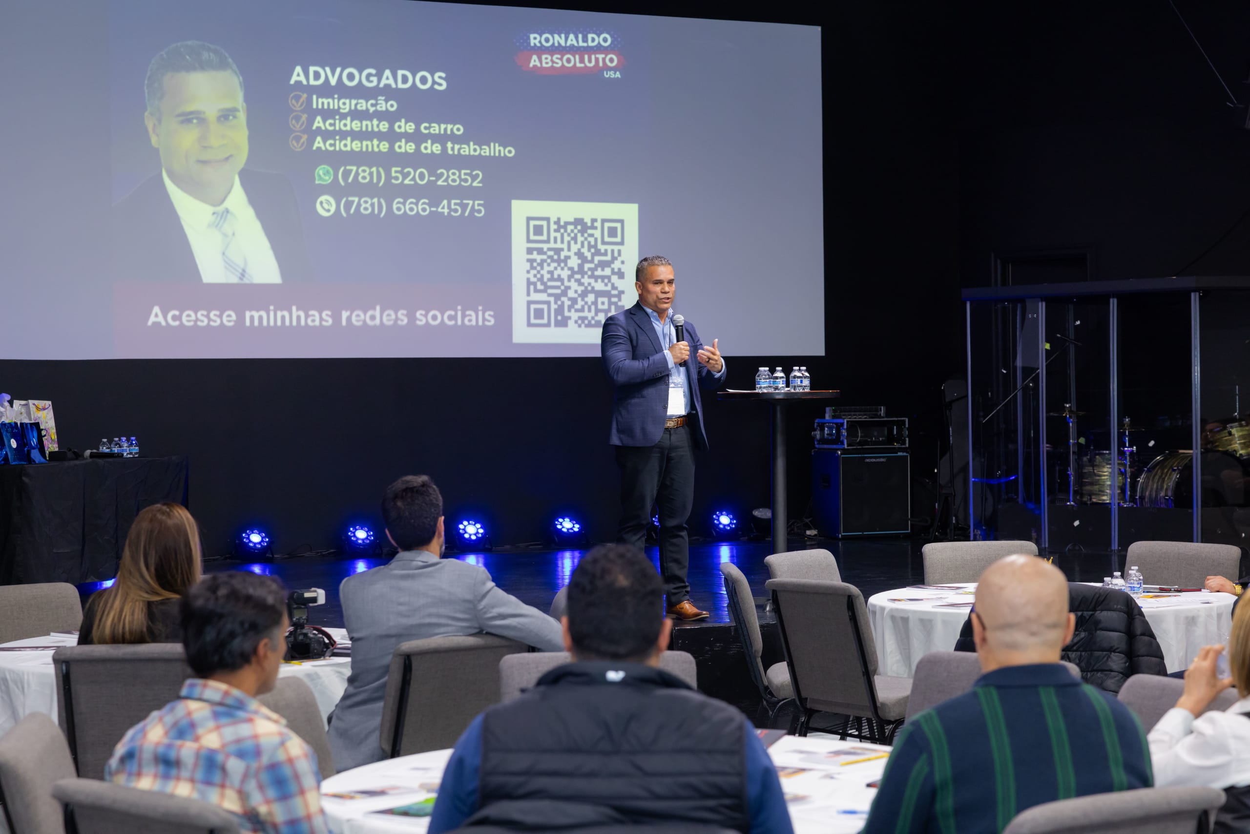 Palestrante no palco diante de um telão com o anúncio de um escritório de advocacia