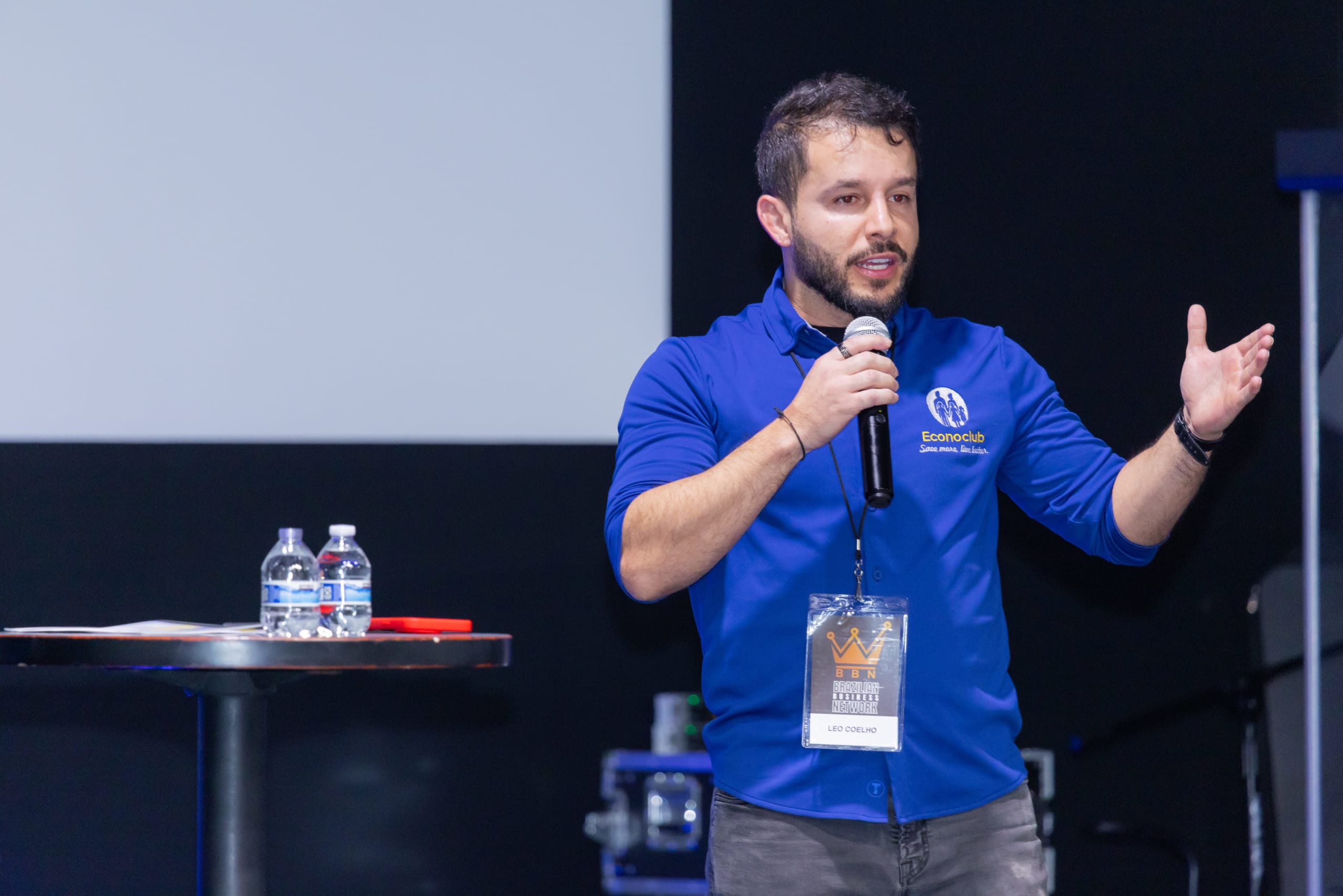 Palestrante de camisa azul gesticula animado enquanto fala ao microfone