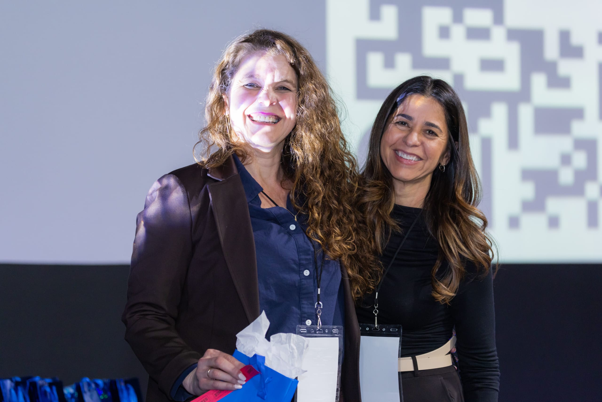 Duas mulheres sorriem abraçadas no palco