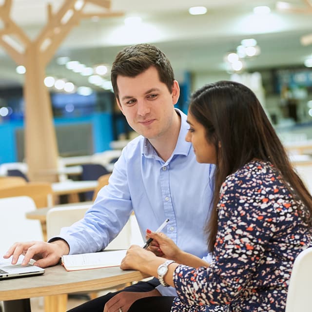 Male and female Nestle Tech employees talking about work at a table in the office.