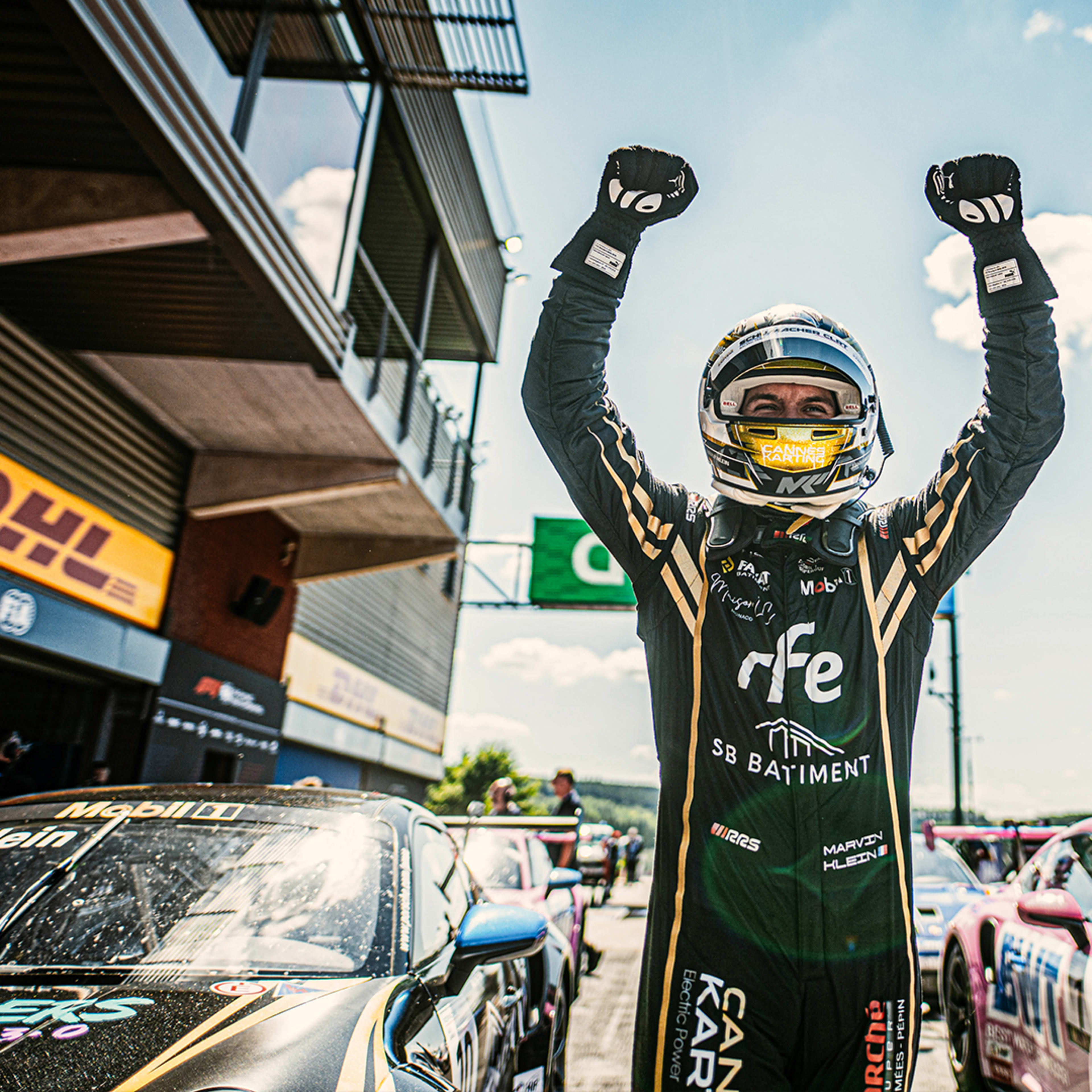 Racing driver Marvin Klein throws his hands in the air in front of his racing car after his victory in the 2024 Porsche Supercup race in Spa-Francorchamps