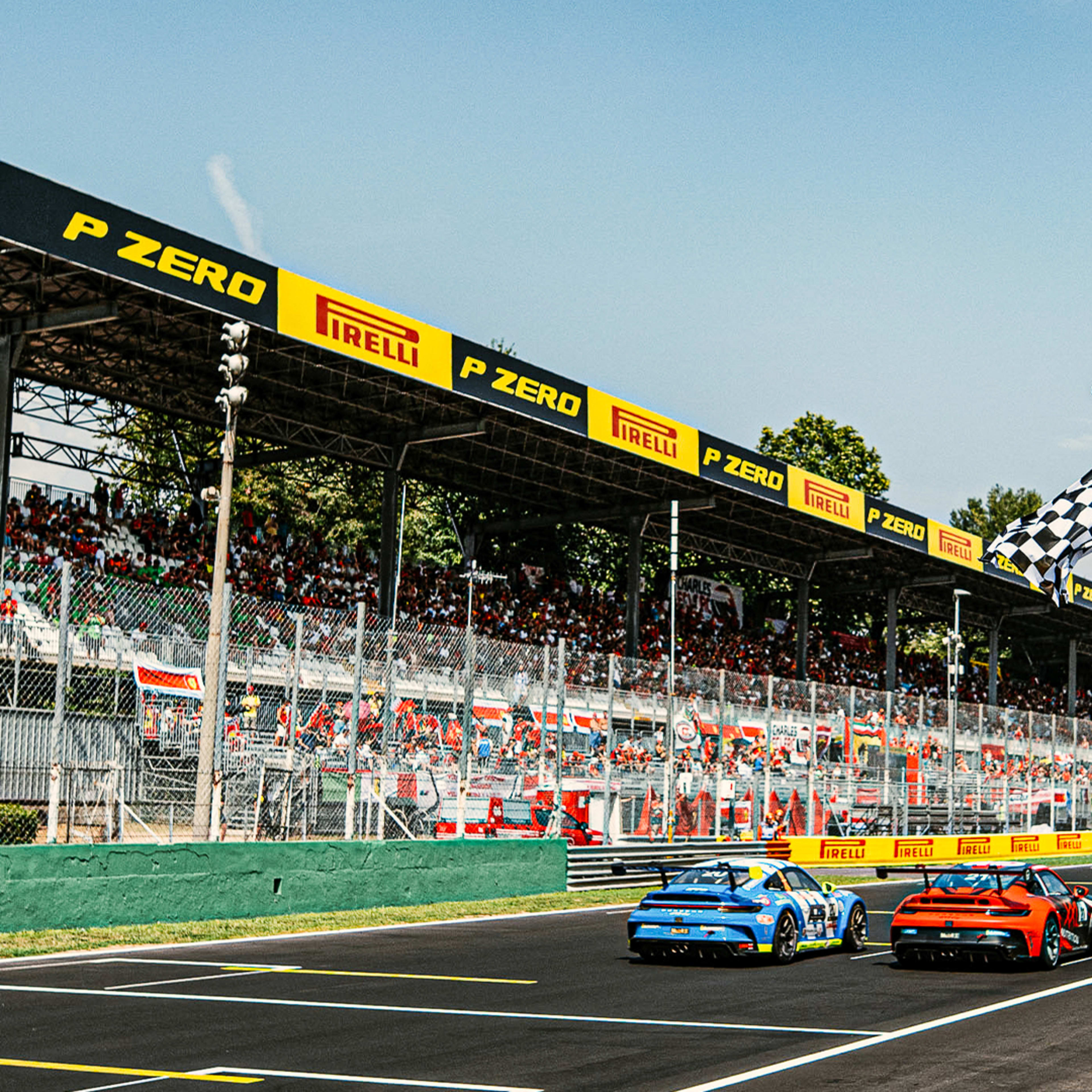 Two Porsche 911 GT3 Cup side by side racing down the home straight in Monza, the chequered flag is waved in the foreground