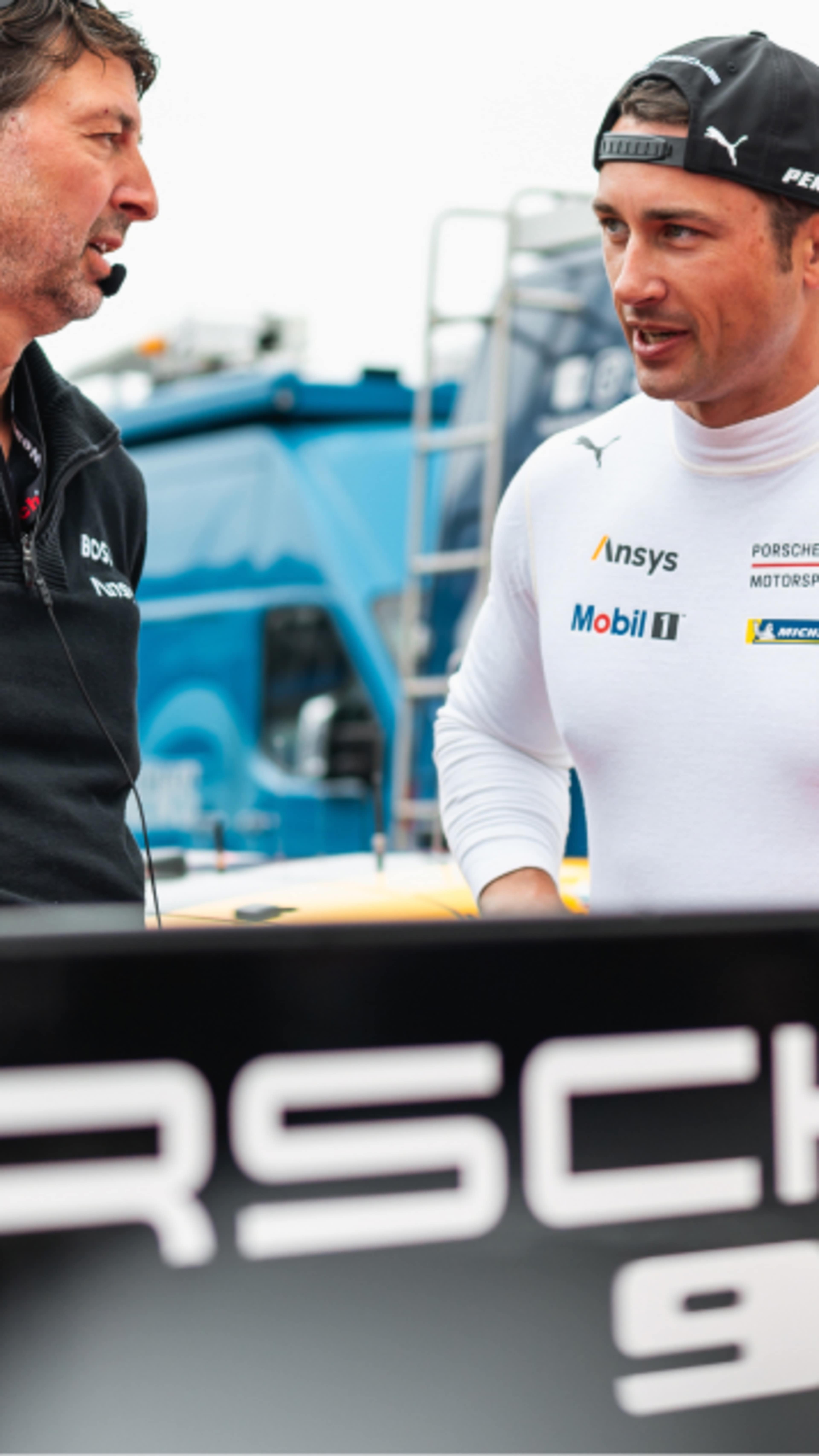 Dane Cameron talking to his colleague behind a Porsche 963 banner 