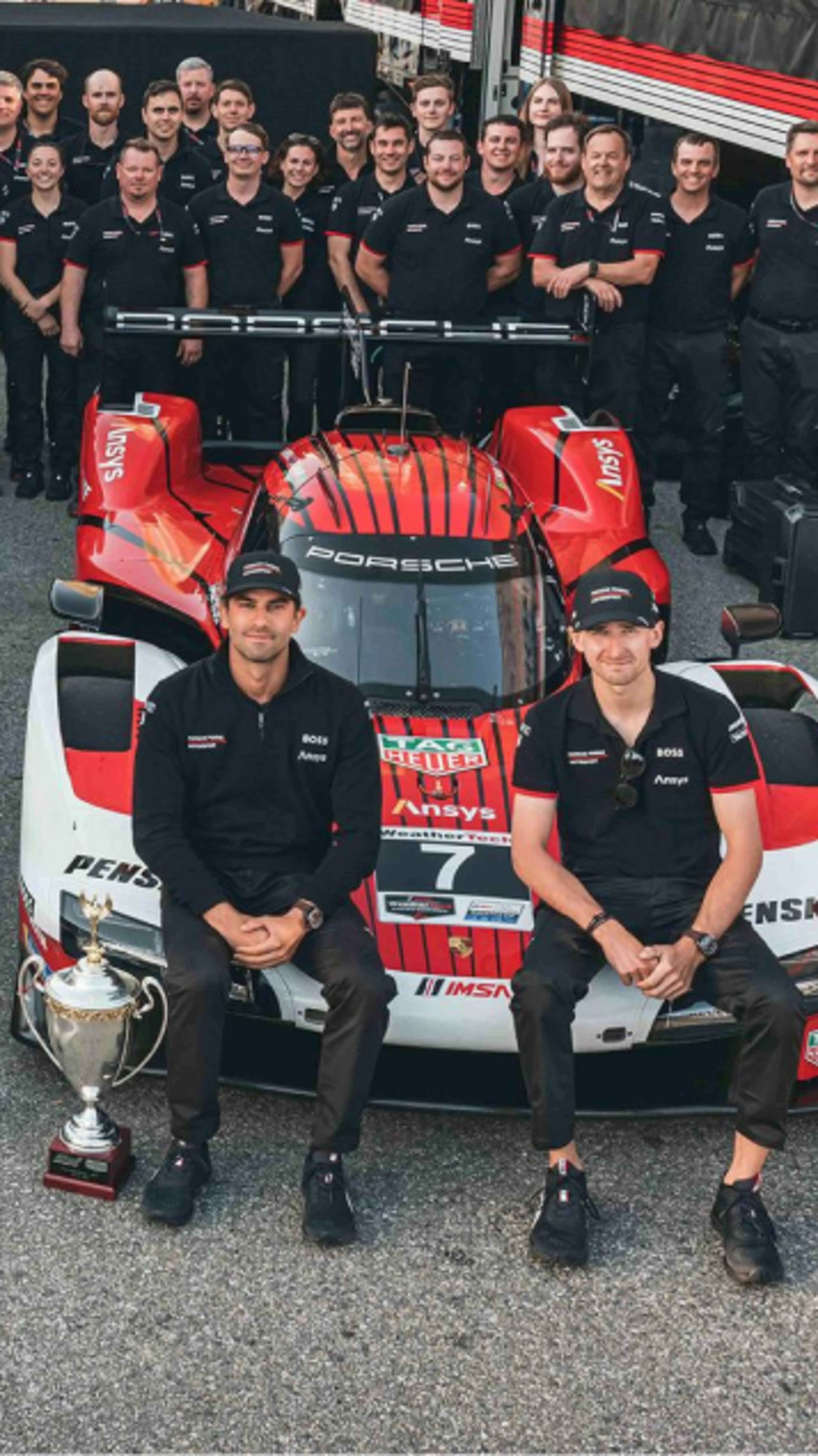 Two Porsche cars with drivers and colleagues sitting on the front and trophies in the middle
