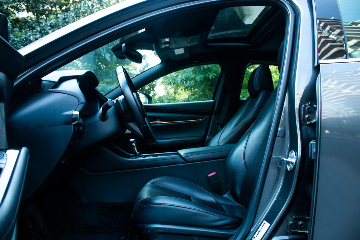 Mazda 3 2.5 2024 - Vista interior de sedán color gris oscuro, con asientos de cuero negros y techo panorámico en exterior.