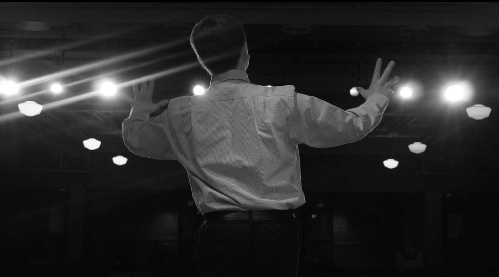 A performer on stage, arms raised under the lights