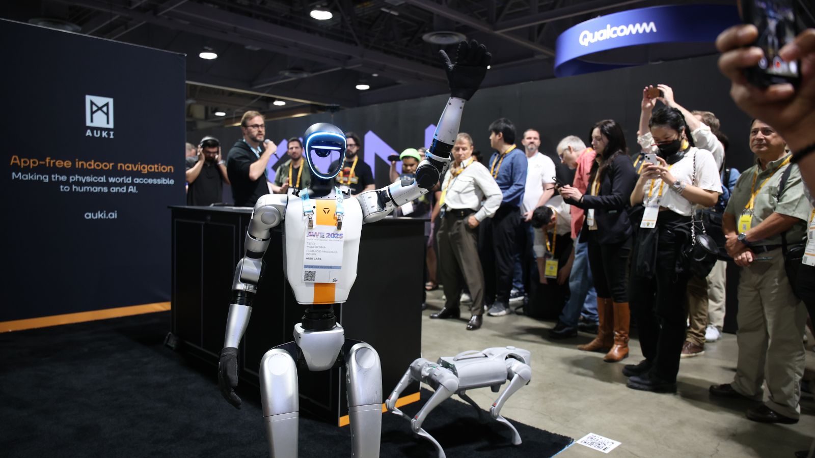 A humanoid robot waving next to a robotic dog at an expo booth
