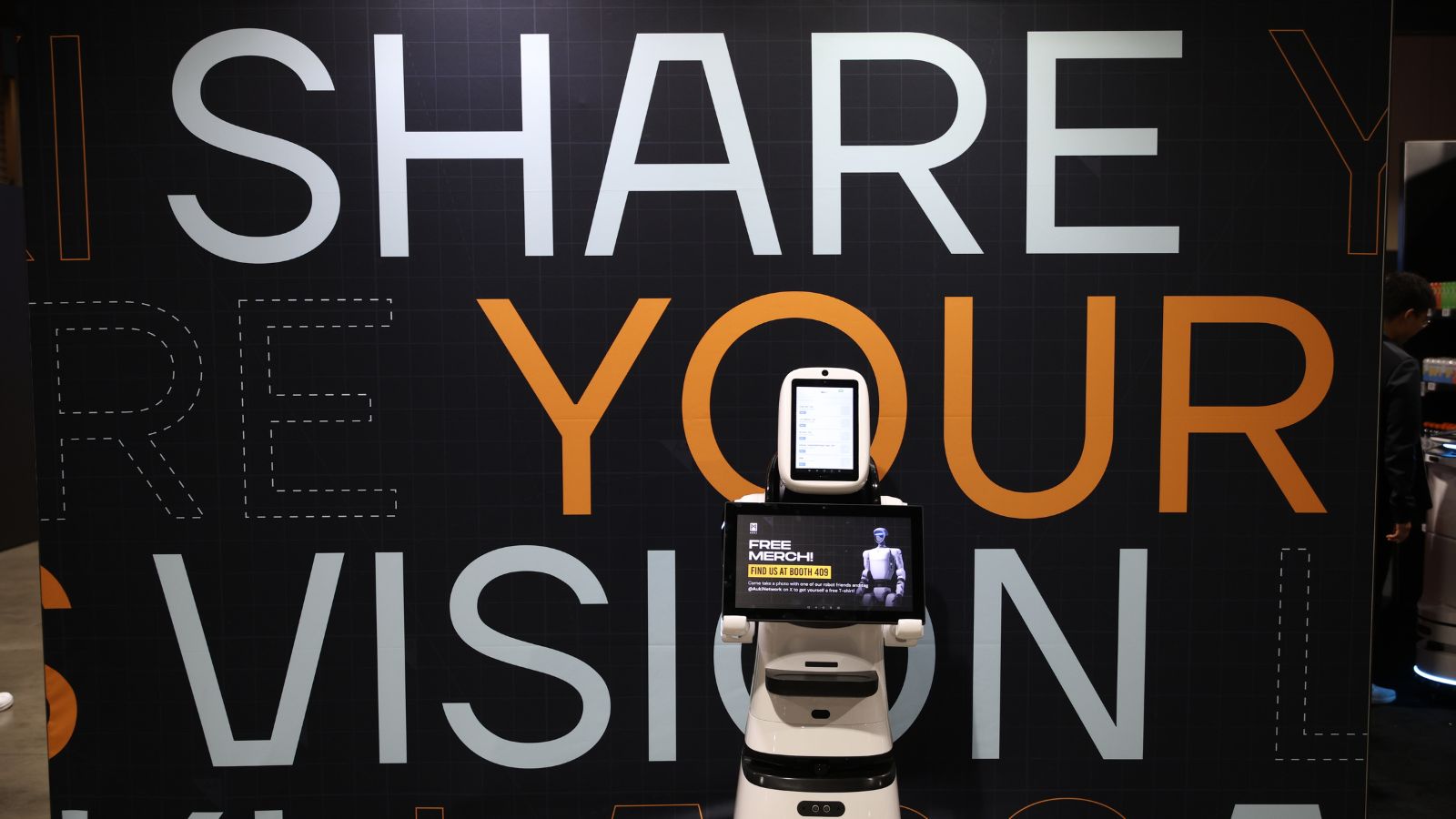 Small robot displayed in front of a Share Your Vision backdrop