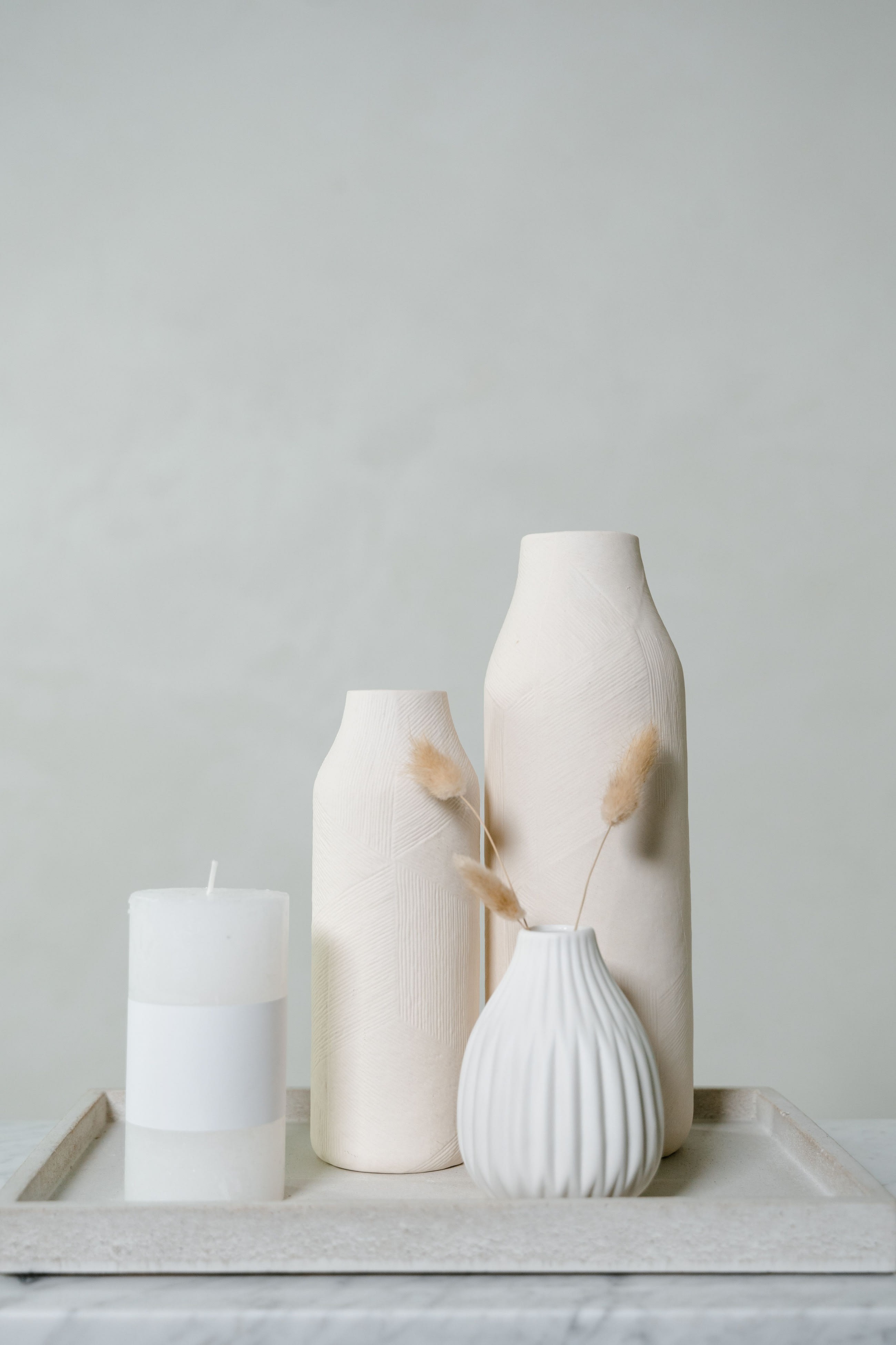 The four pieces of The Collection styled on a stone tray: a white pillar candle, two etched stoneware vases and a pleated porcelain bud vase