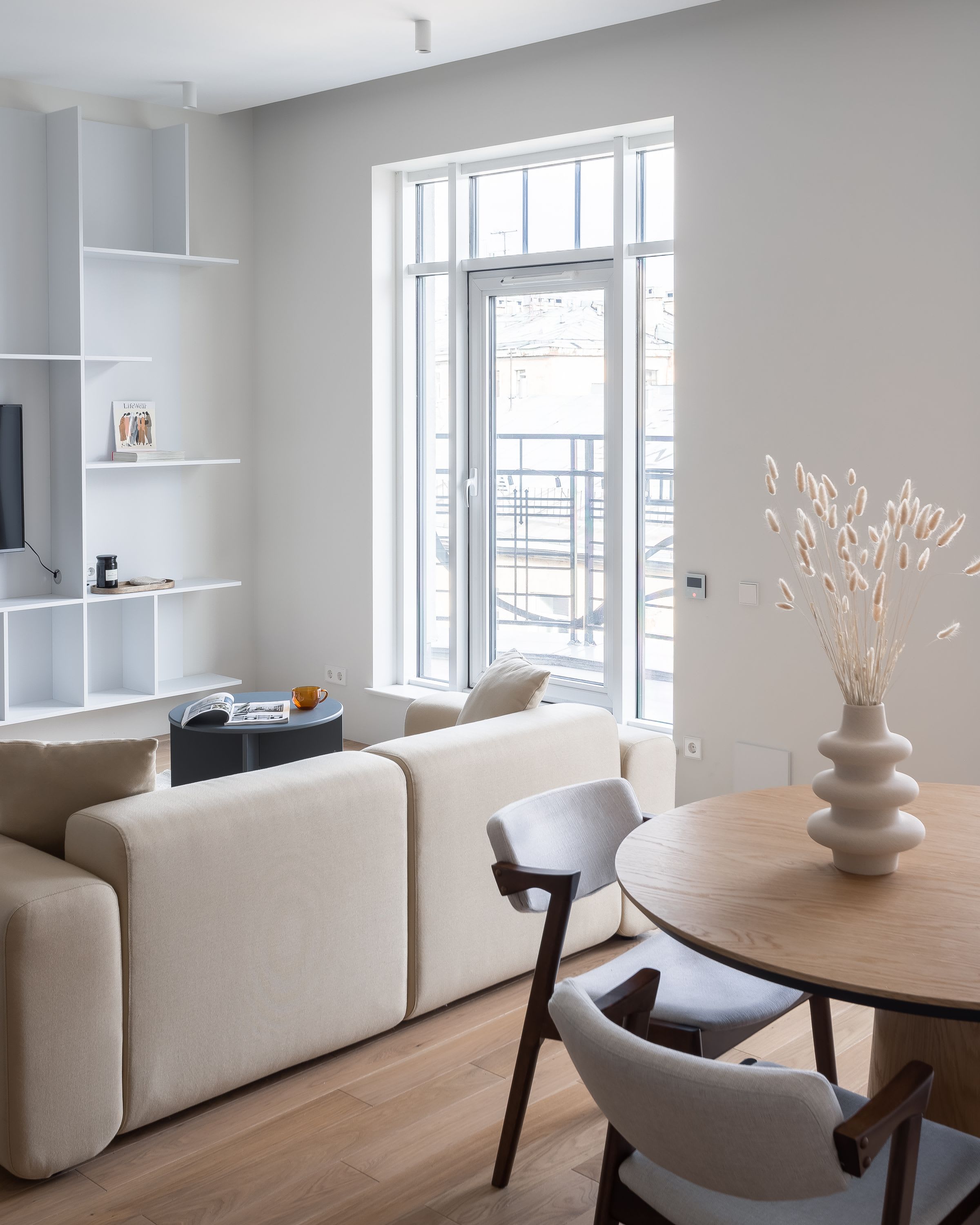Calm living room with a cream sofa, round wooden table and a white vase of dried grasses