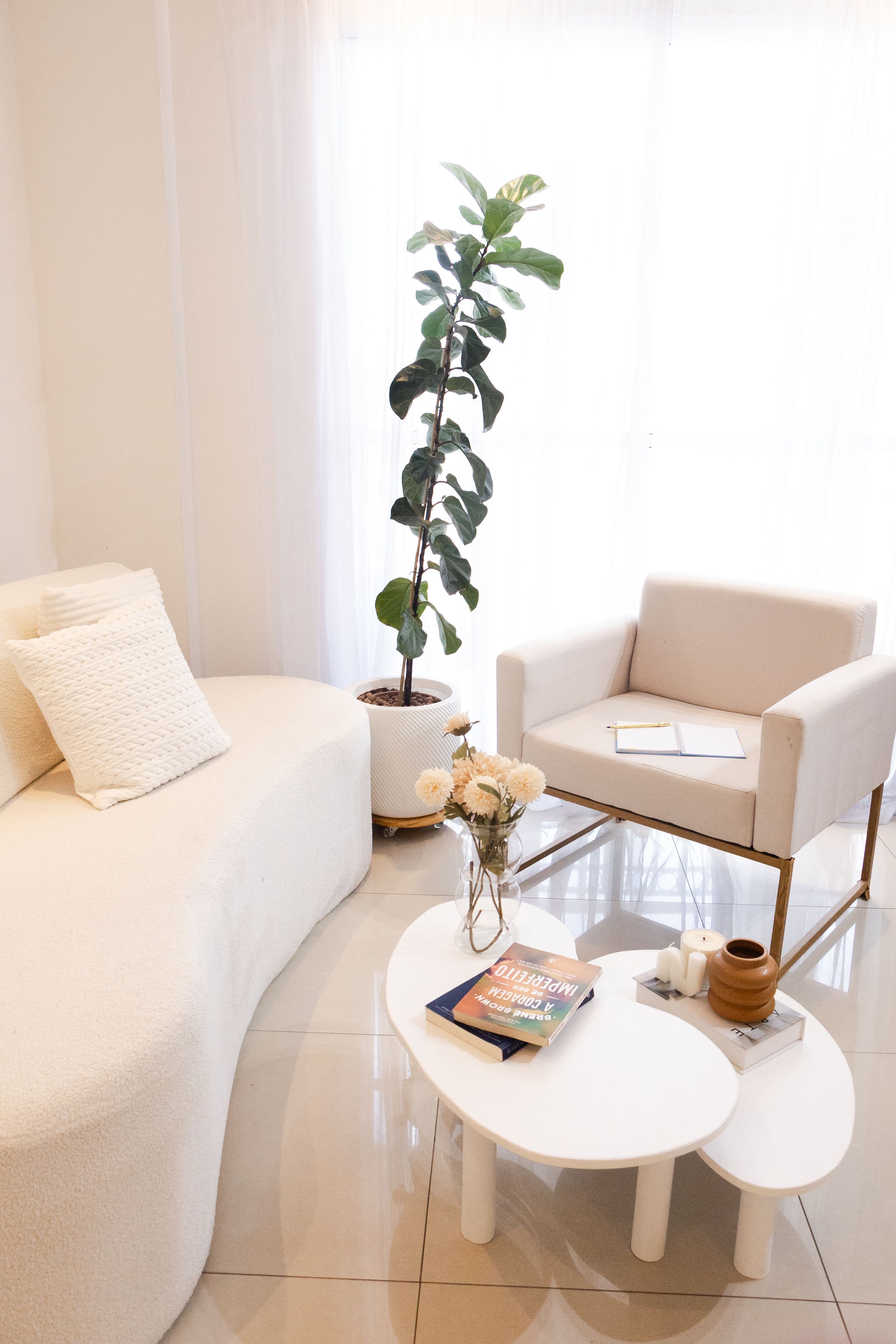 Bright living room with a curved white sofa, an armchair and a fiddle-leaf fig by the window