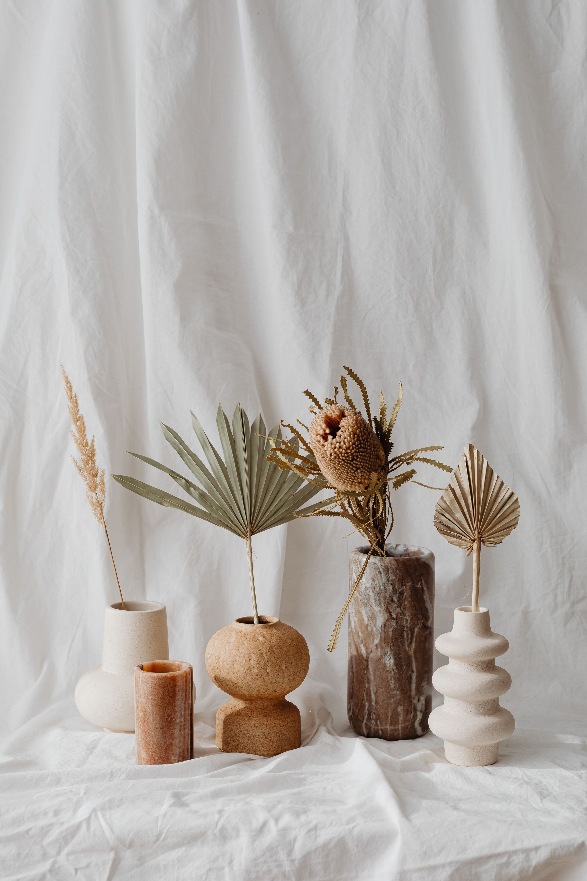 Ceramic vases with dried palm leaves and seed heads on draped white linen