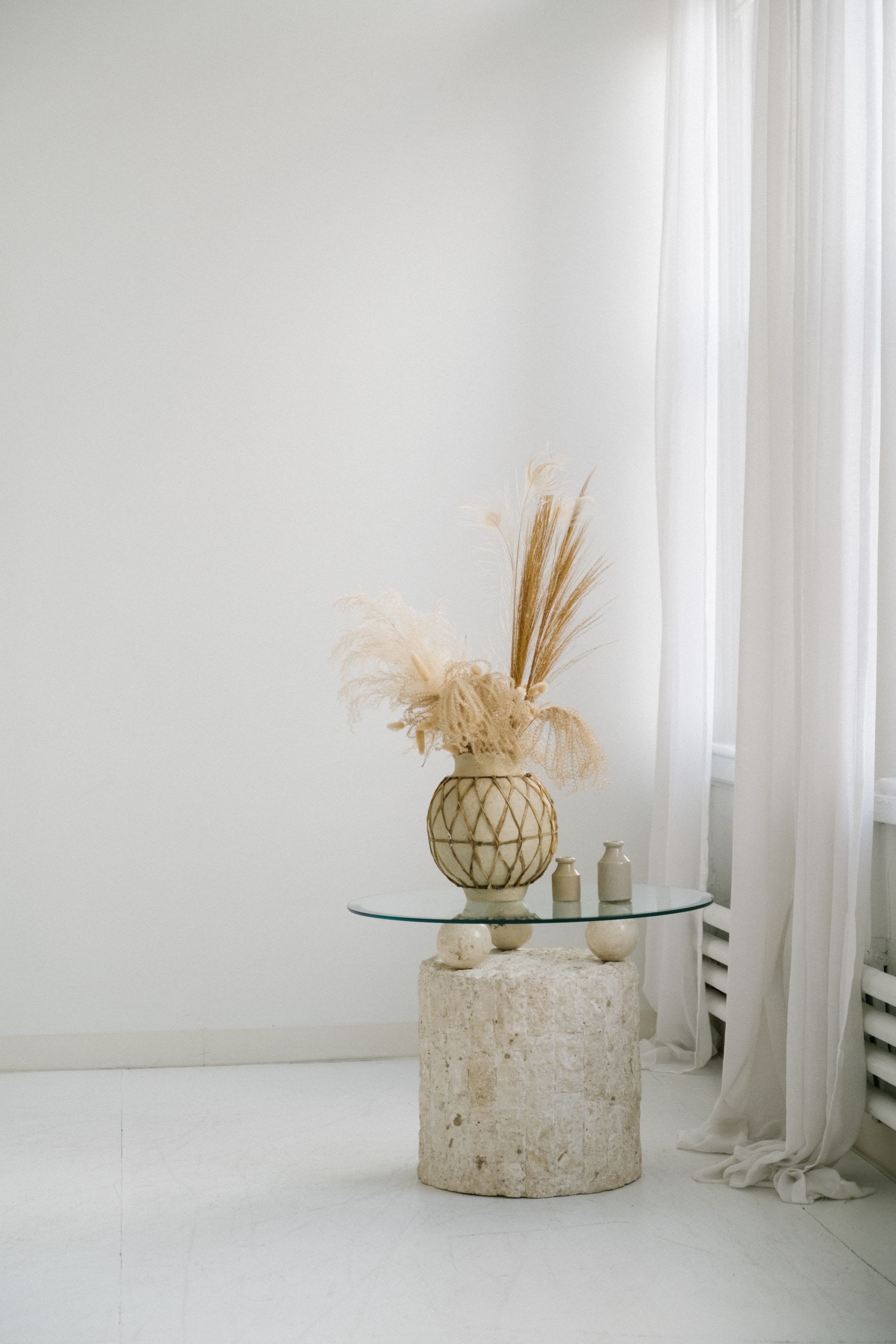 A bright room with dried pampas in a vase on a small stone side table