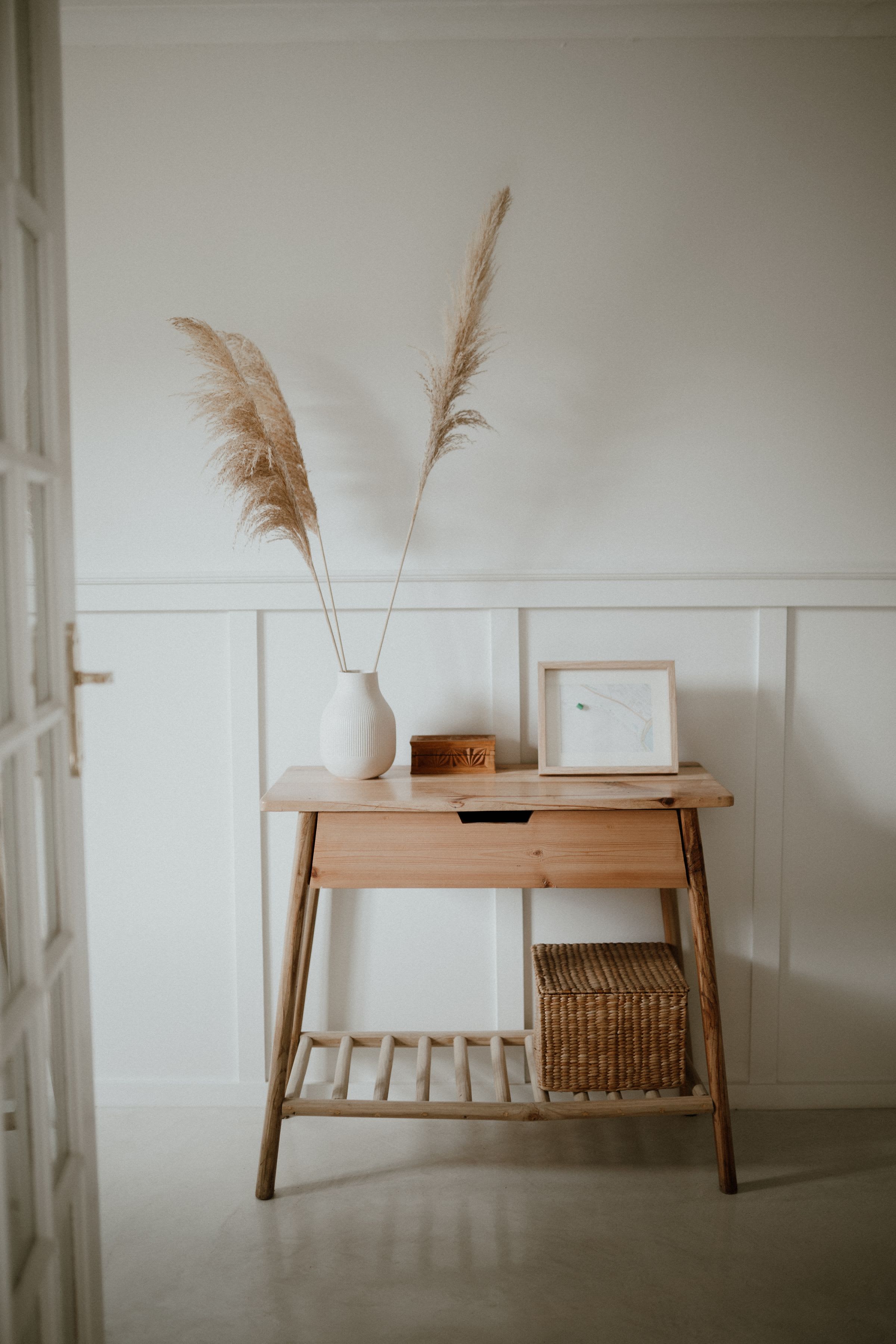 A wooden console styled with pampas grass, a framed print and a woven basket