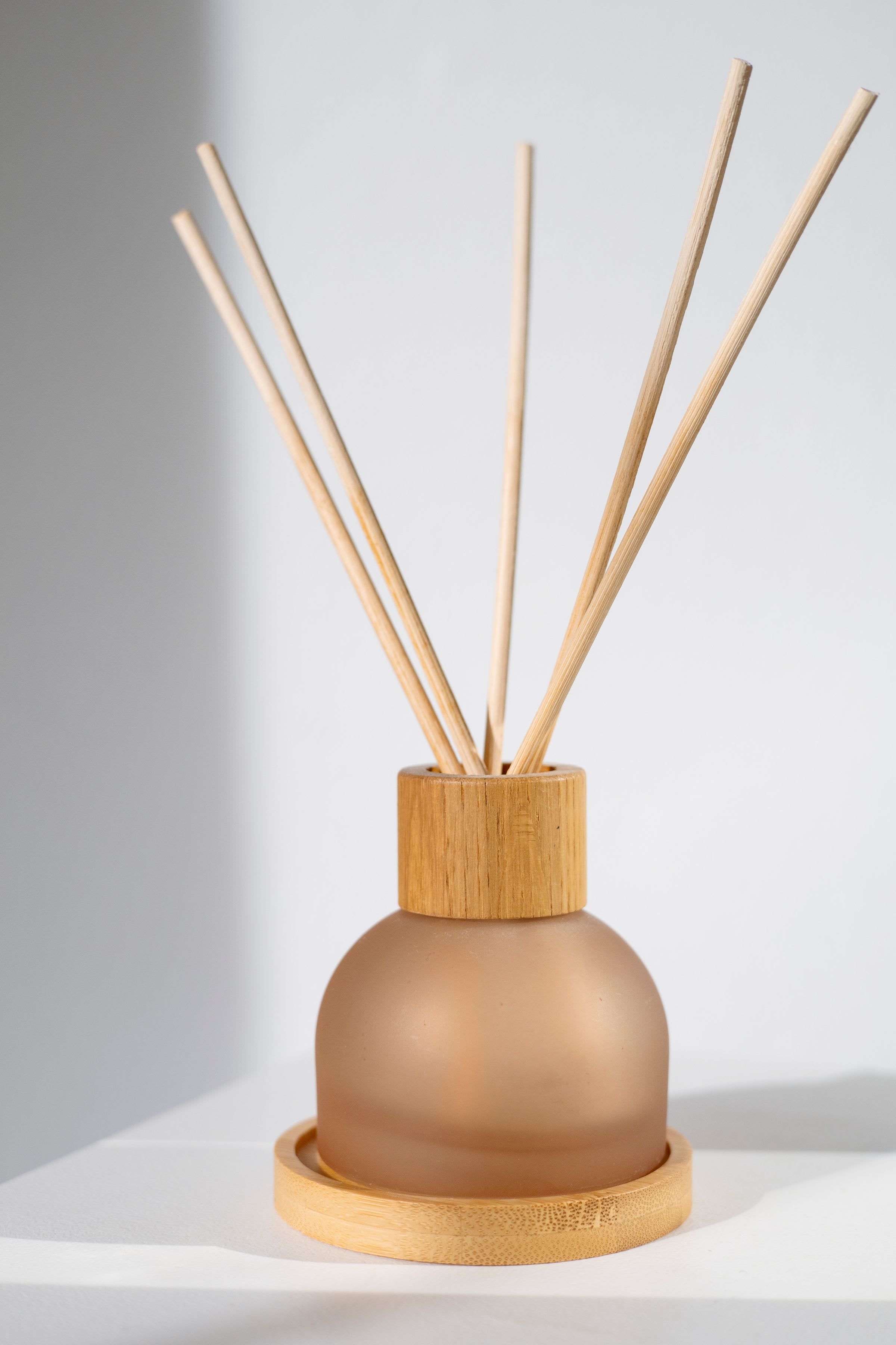 Reed diffuser in frosted glass with a turned wooden collar and rattan reeds