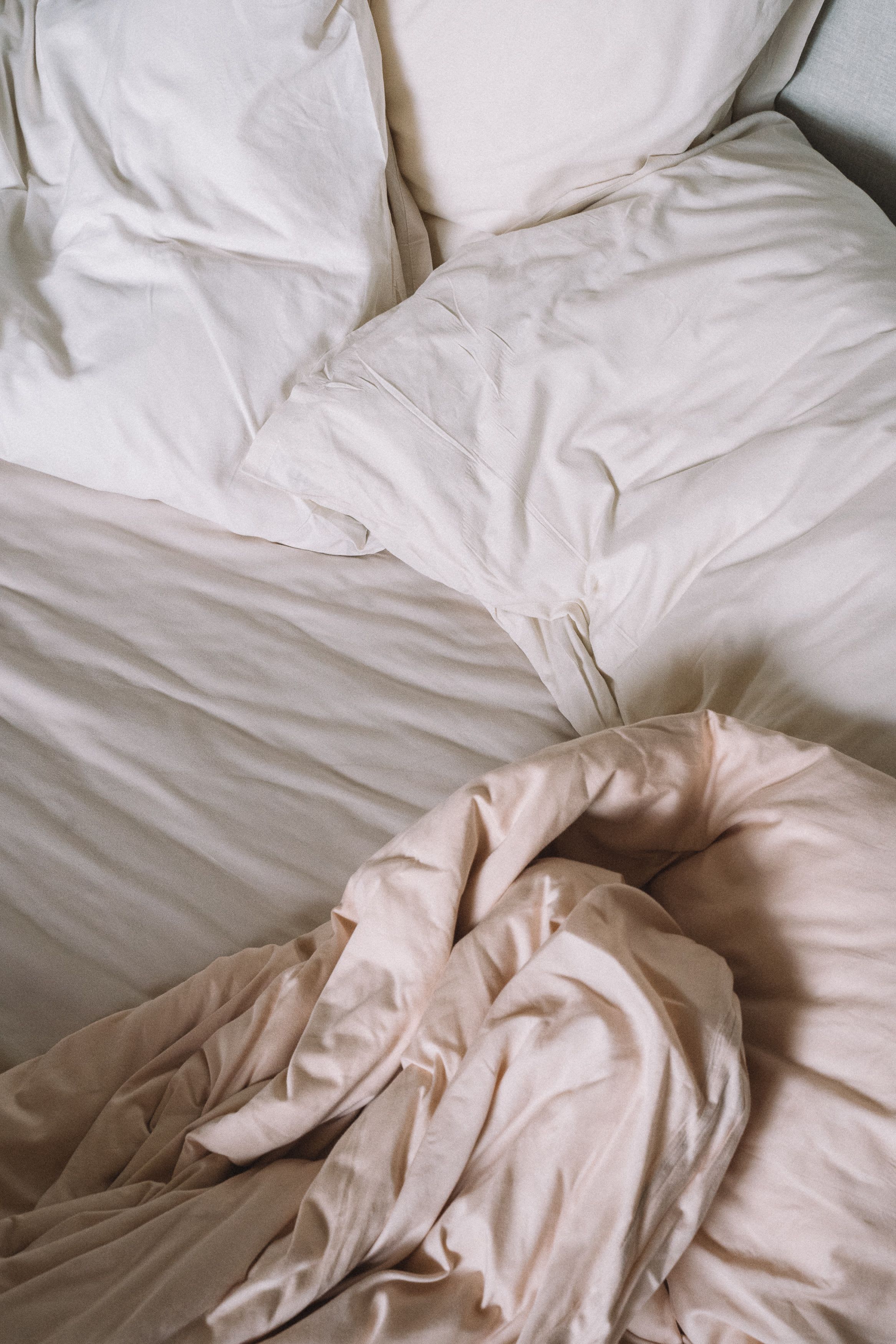 Unmade bed dressed in soft oat-coloured linen