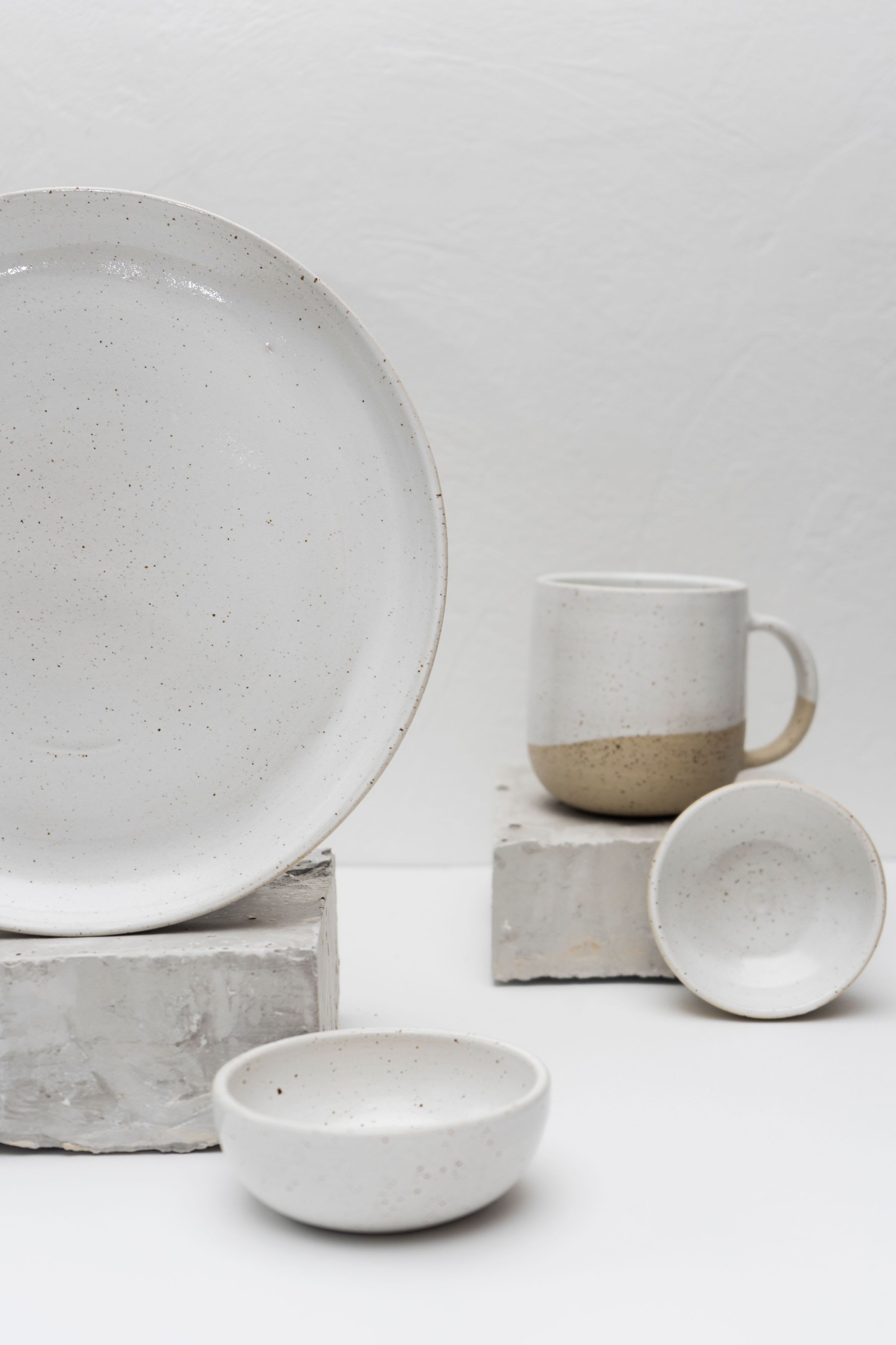 Speckled white stoneware plate, bowl and cup arranged on concrete blocks