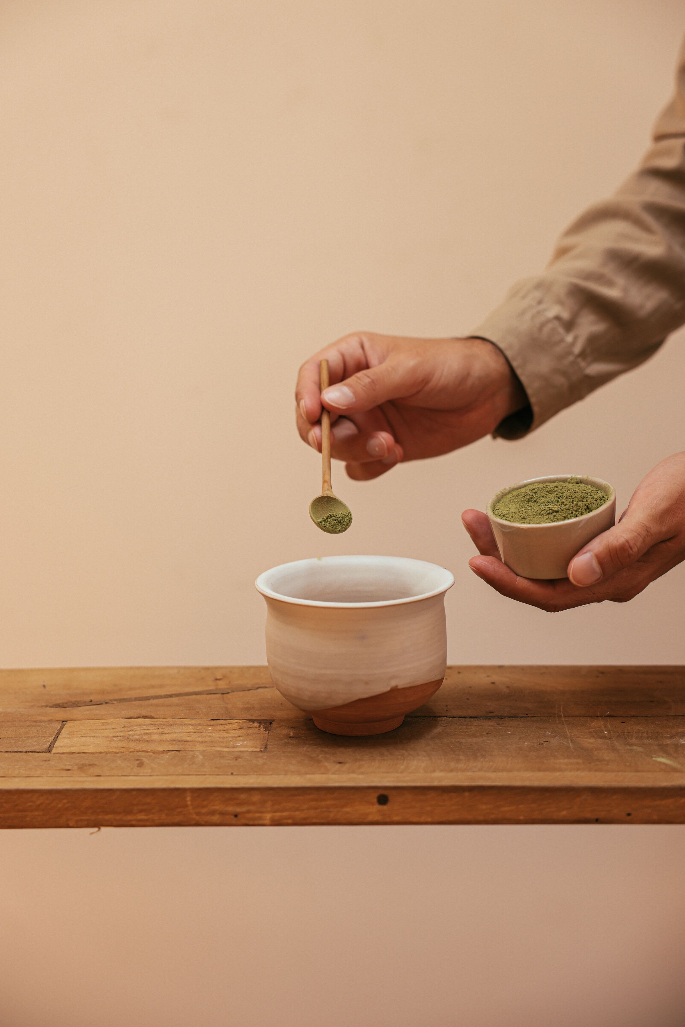 A spoonful of loose leaf tea being lifted into a cup against a warm beige wall