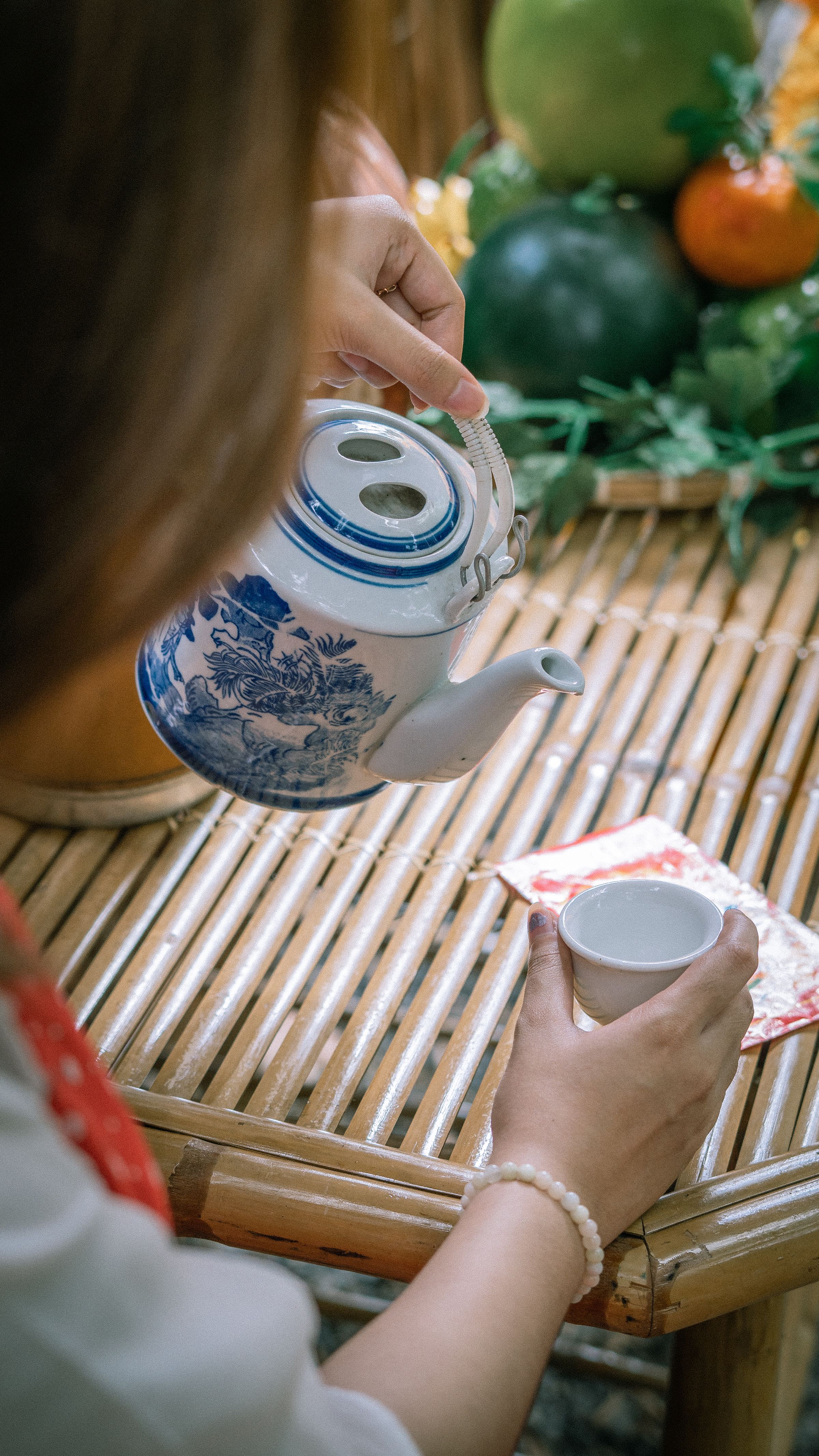 A woman pouring tea from a blue patterned teapot at a bamboo table