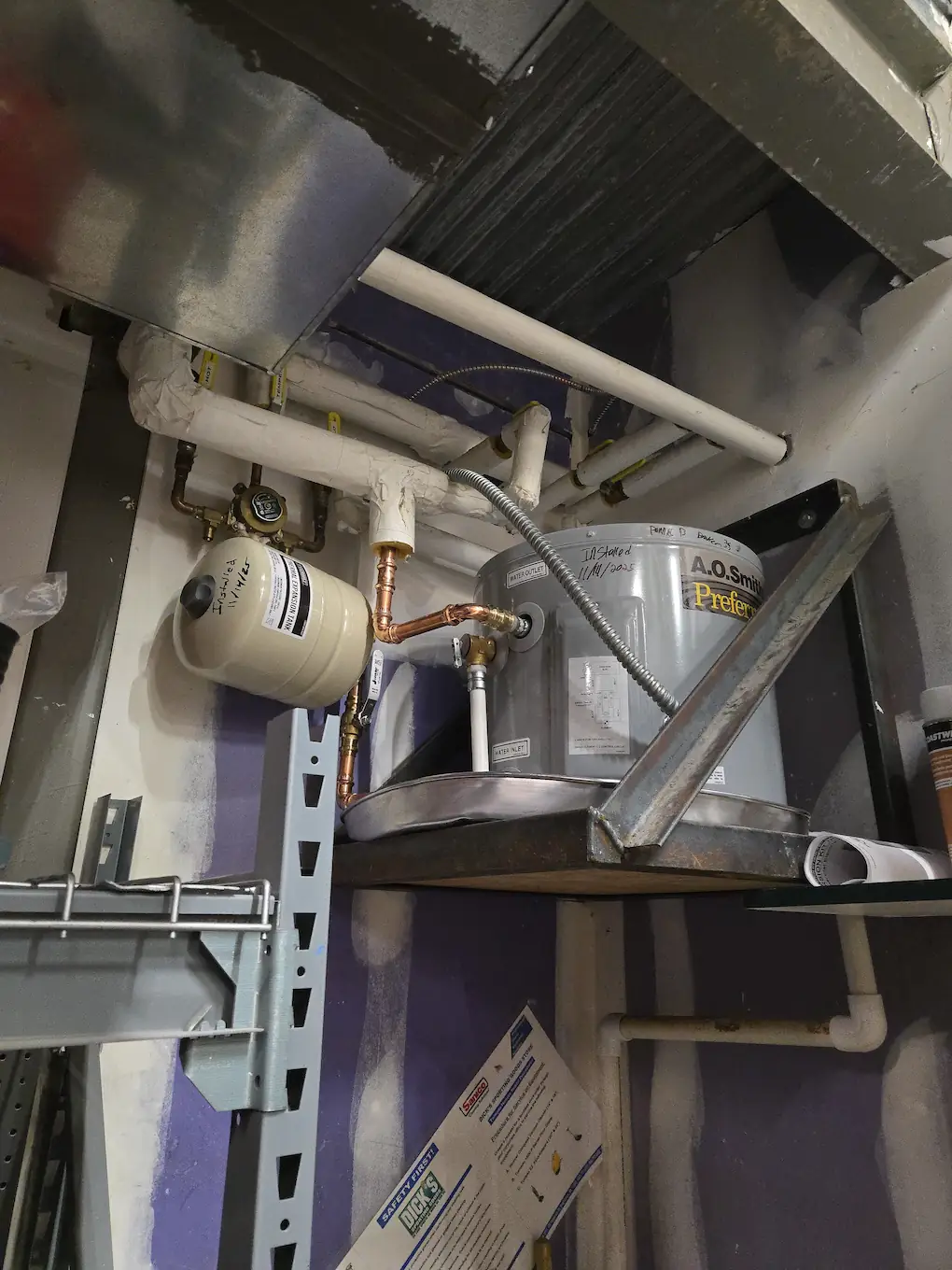 Compact commercial AO Smith water heater elevated on a metal shelf with expansion tank and copper piping