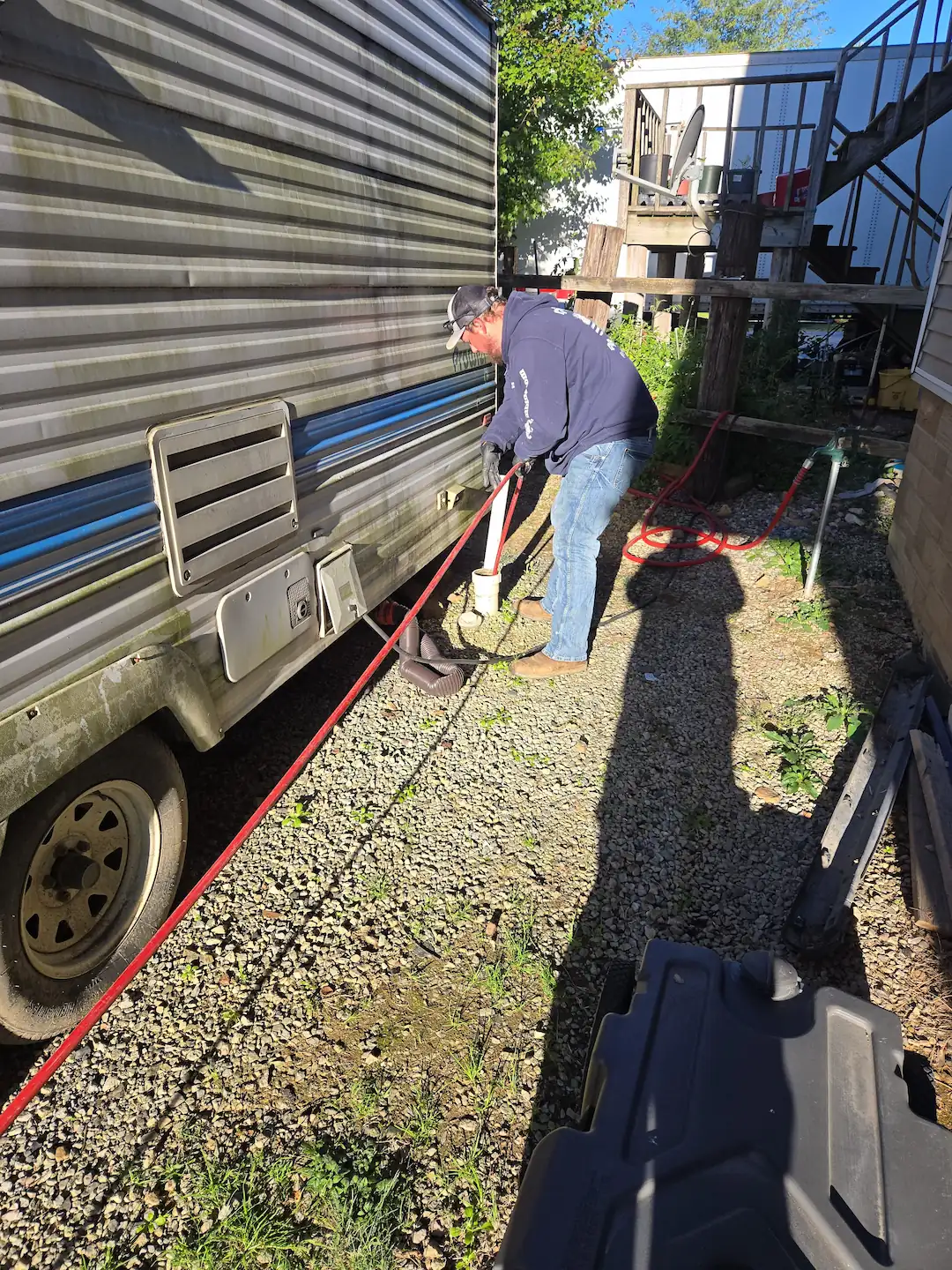 Technician in Aspers feeding a red hydro-jet hose into an RV cleanout beside a trailer