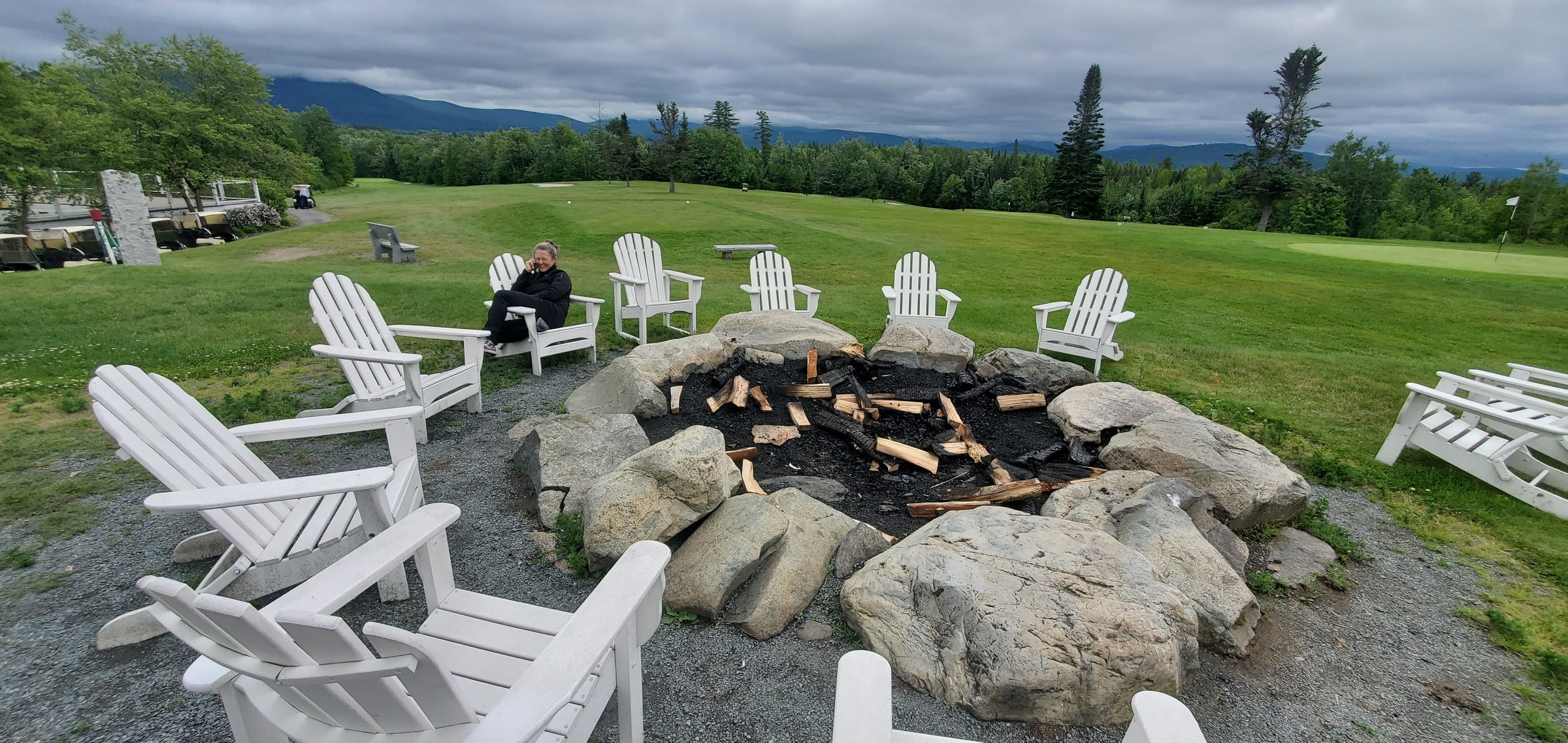 Adirondack chairs around the stone fire pit with mountain views