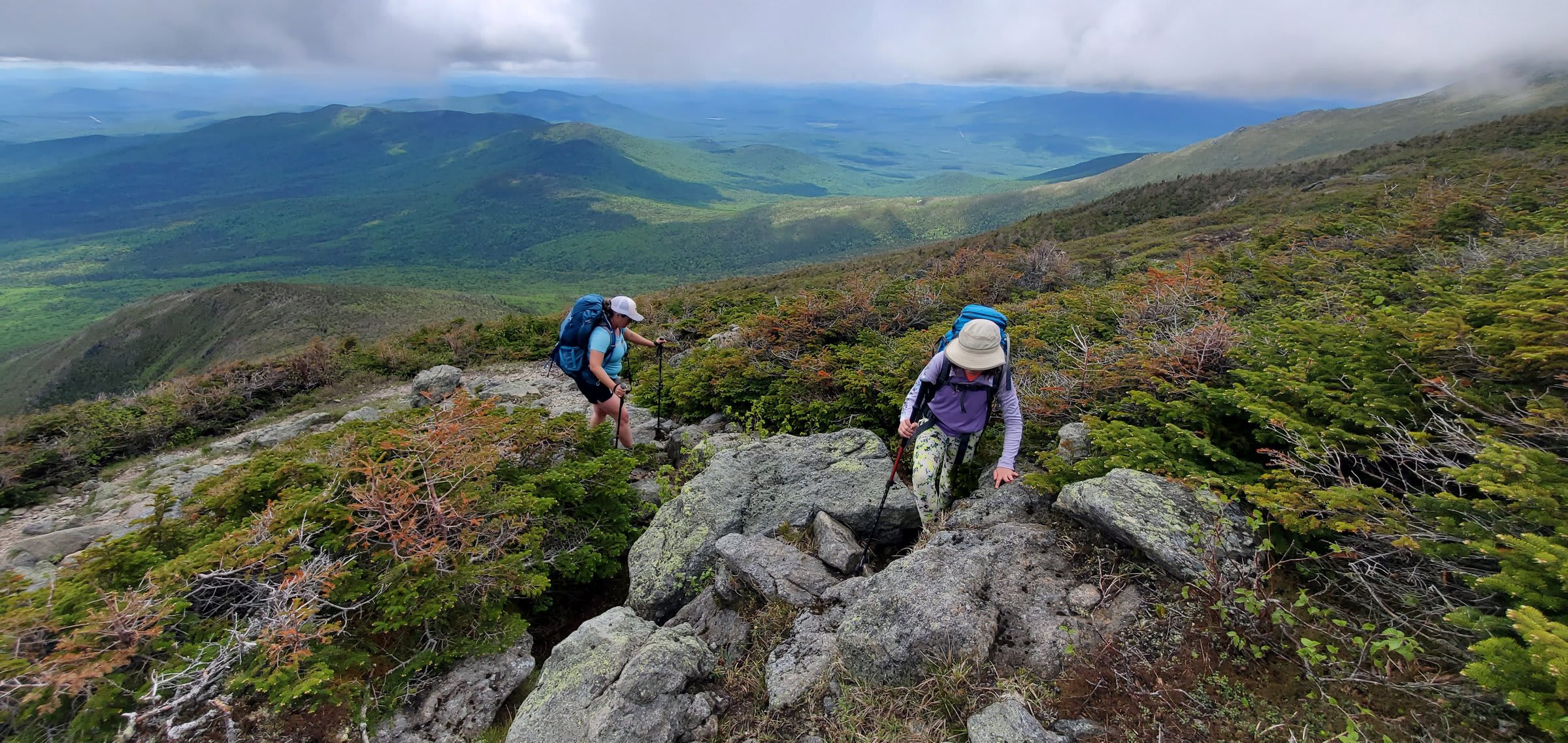 Hikers climbing the rocky ridge above treeline with the valley far below
