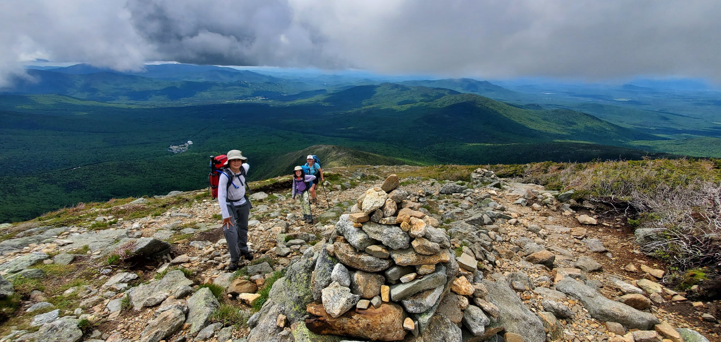 Three backpackers pausing beside a rock cairn on the ascent