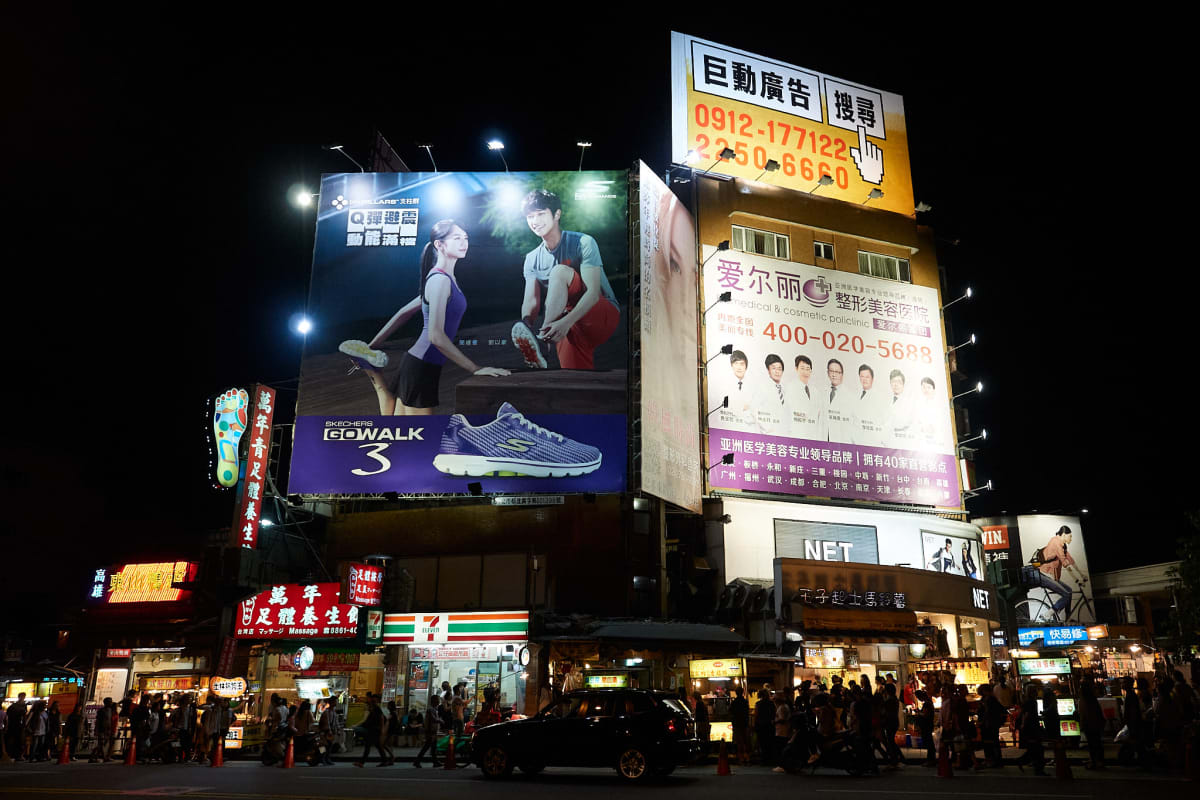 A building rises up from a sea of people with ads covering its sides.