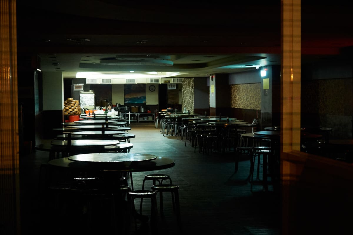 A worker sits at a table in the far back of a restaurant closed for the night.