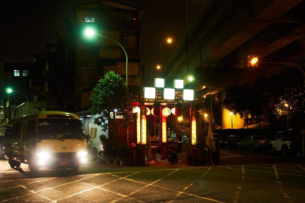 A small bus drives past a shrine adorned with lanterns.