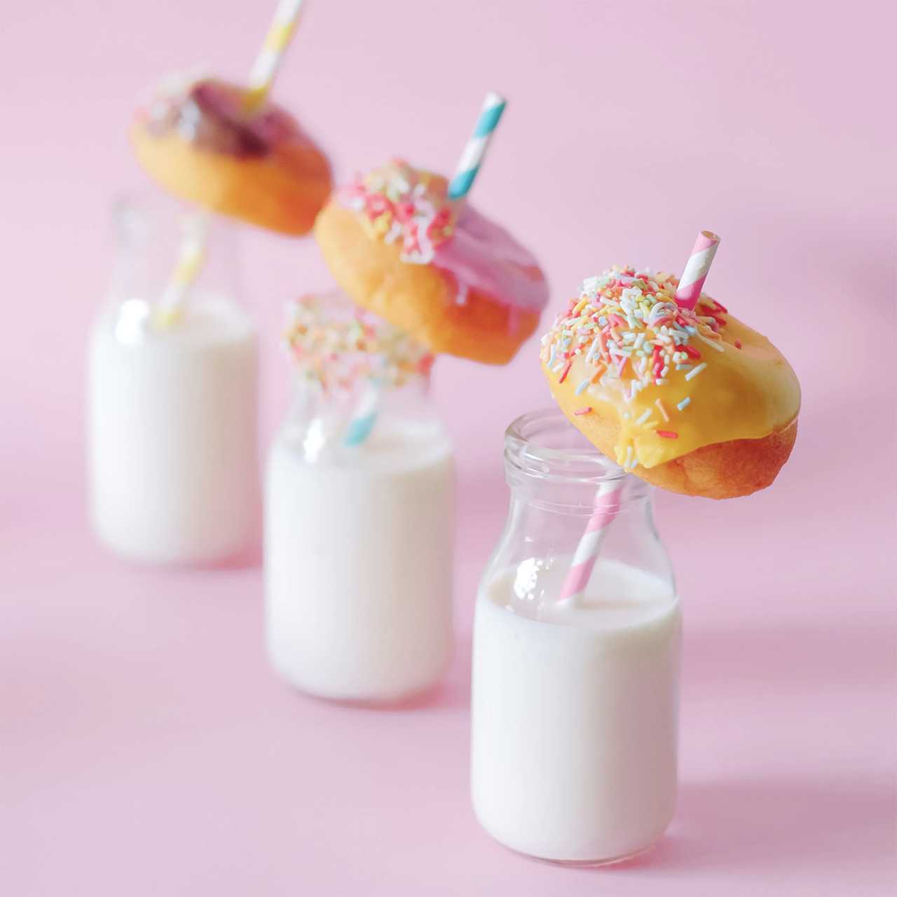 Three bottles of milk, each with straws protruding through donuts.