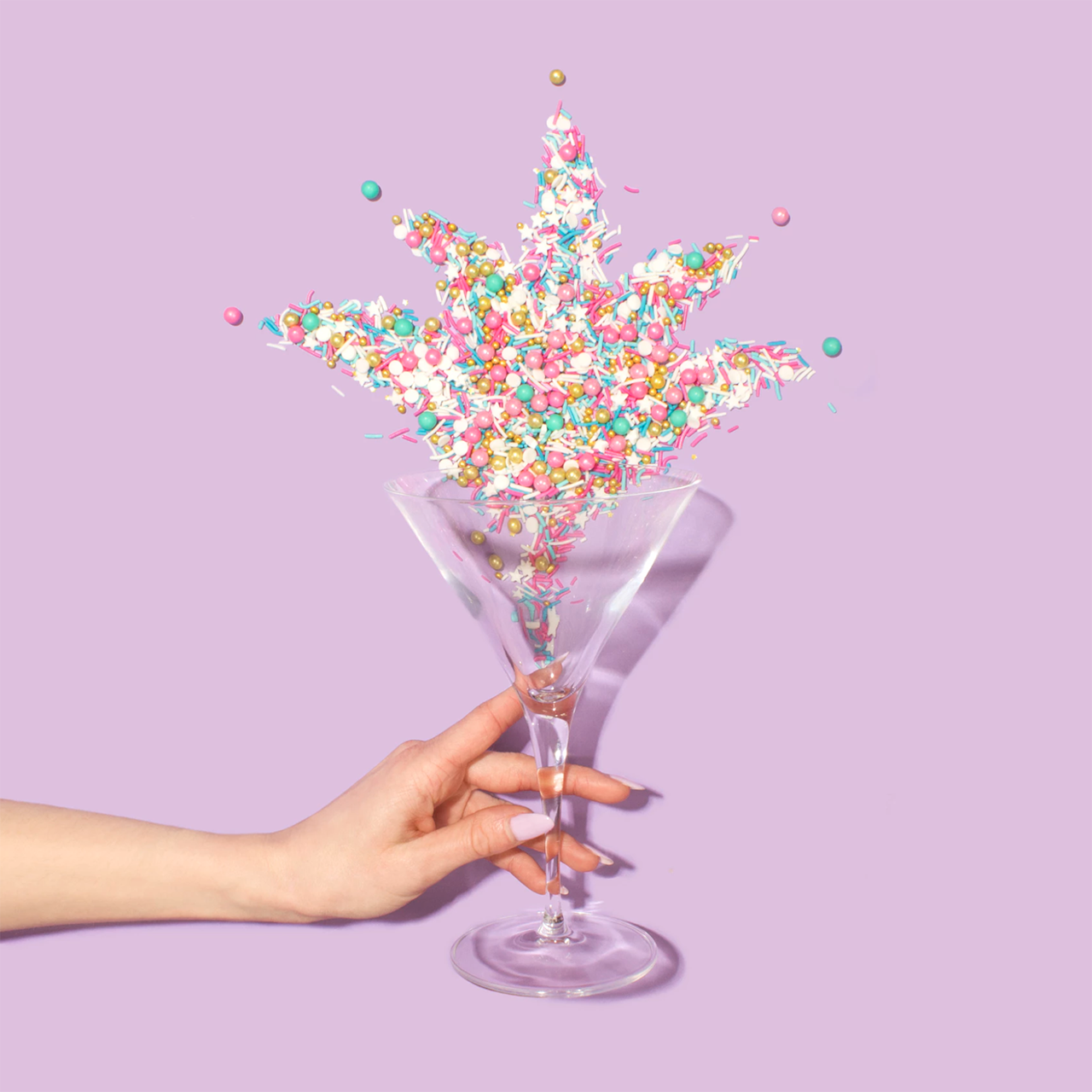 A woman's hand holding a martini glass that is overflowing with candy sprinkles.