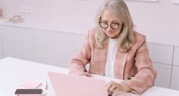 an elderly woman in a pink suit typing on a pink computer on a pink computer