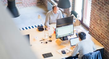 two men sitting in front of computers in an office space