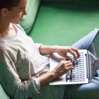 a woman on a green couch typing on a computer